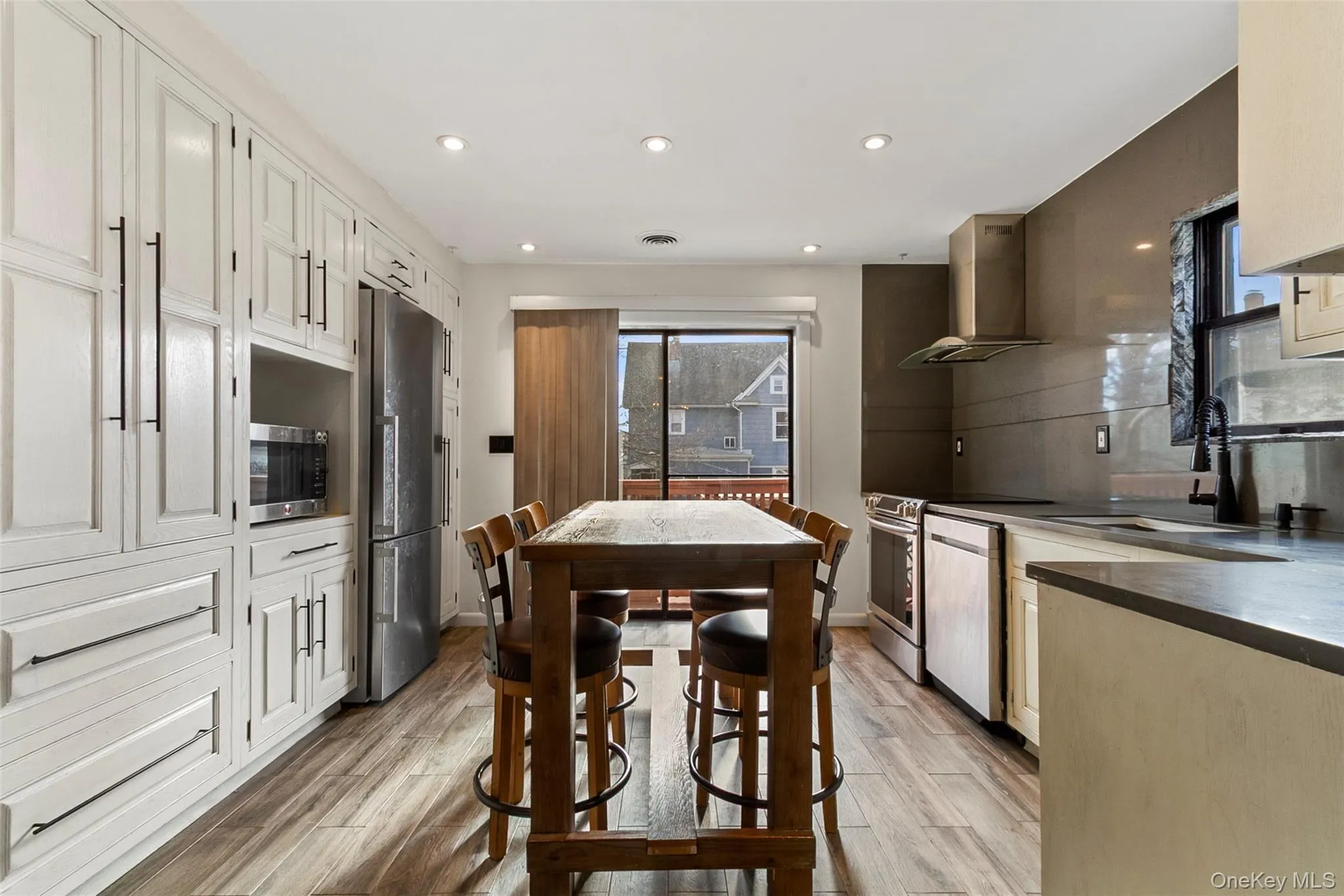 Kitchen featuring recessed lighting, stainless steel appliances, backsplash, and light wood-style flooring with glass door to deck Kitchen featuring recessed lighting, stainless steel appliances, backsplash, and light wood-style flooring with glass door to deck