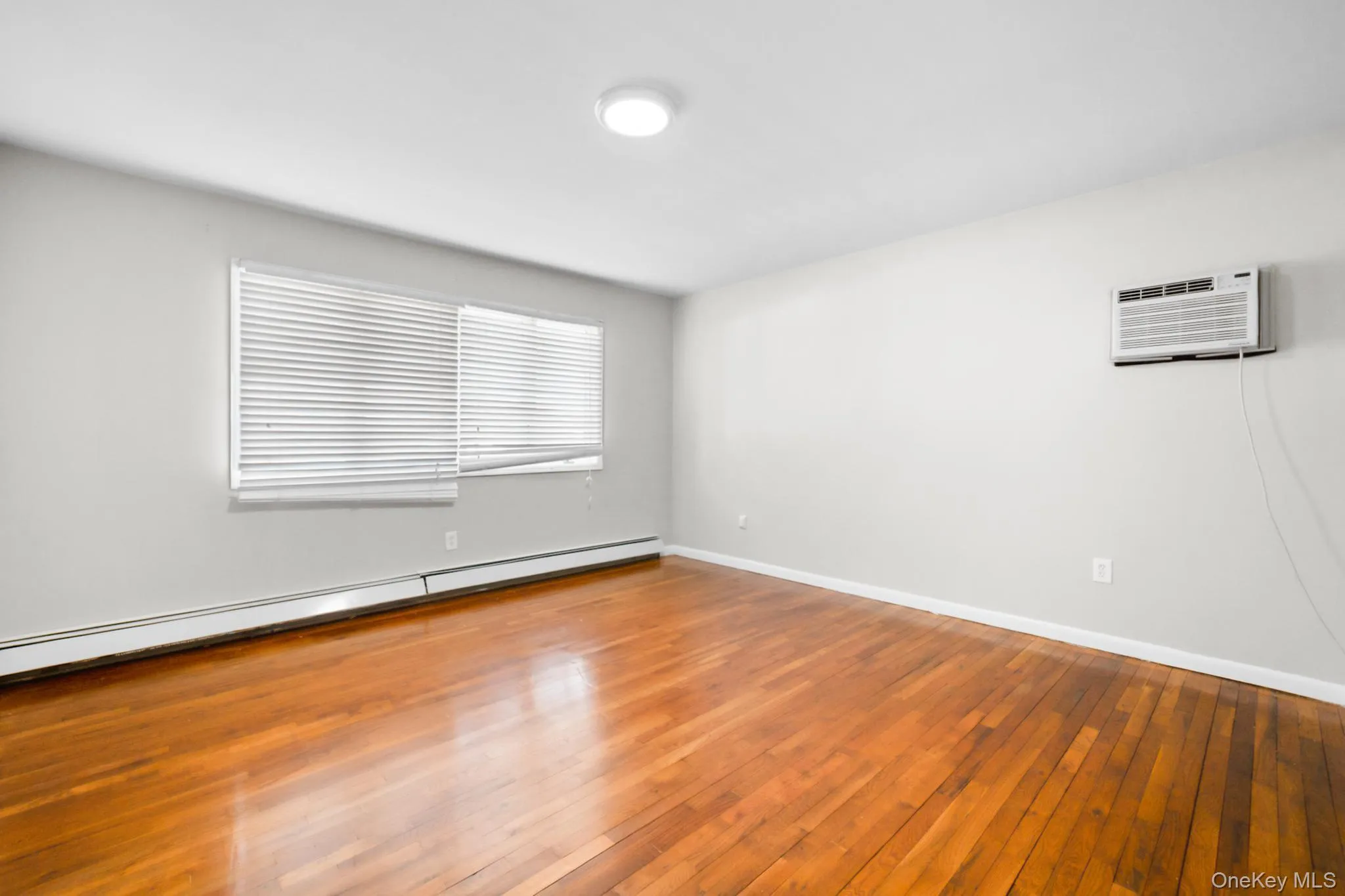 Spare room with a baseboard heating unit, wood-type flooring, and a wall mounted air conditioner Spare room with a baseboard heating unit, wood-type flooring, and a wall mounted air conditioner