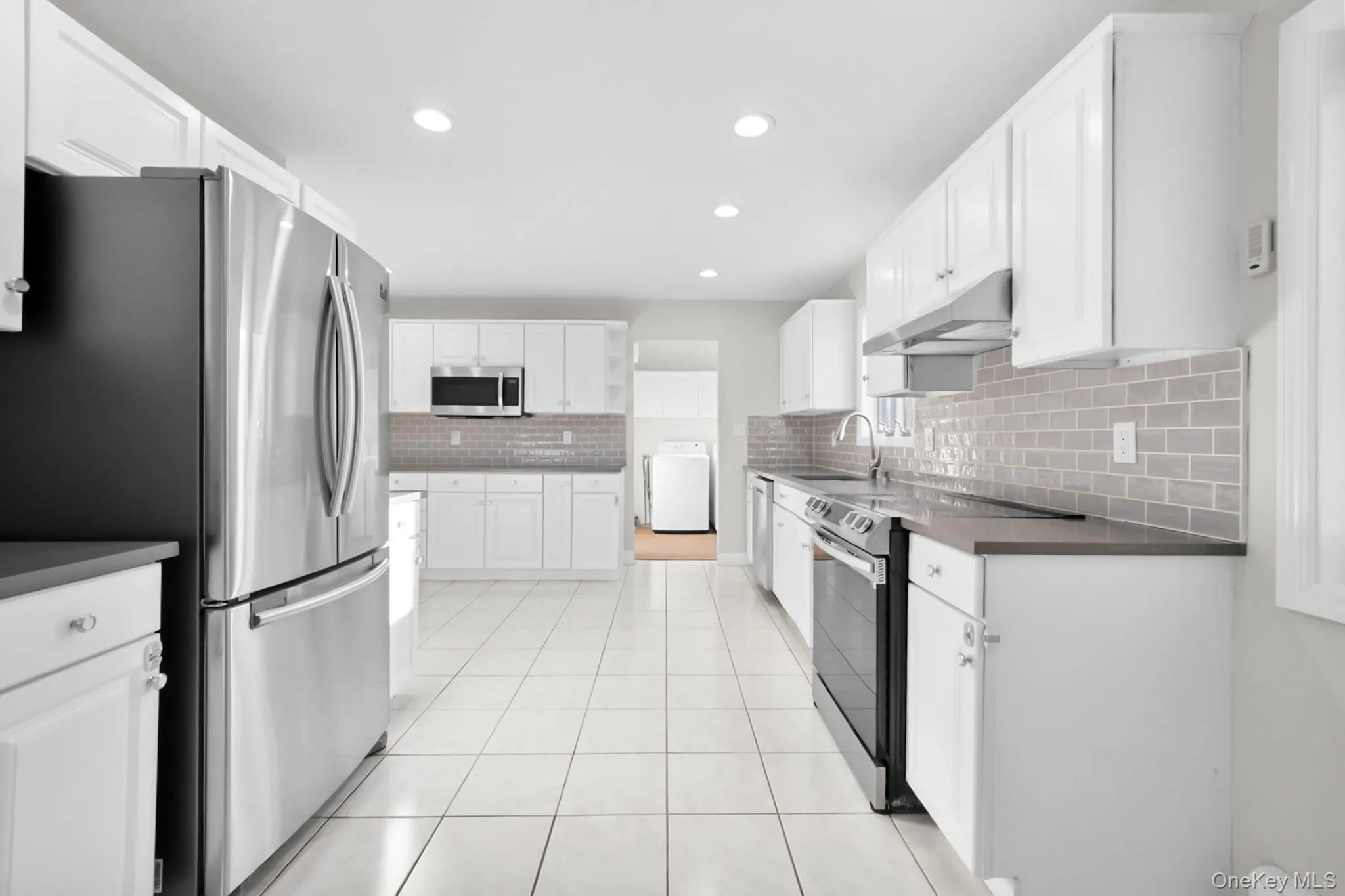 Kitchen with dark countertops, stainless steel appliances, white cabinets, light tile patterned flooring, and recessed lighting Kitchen with dark countertops, stainless steel appliances, white cabinets, light tile patterned flooring, and recessed lighting