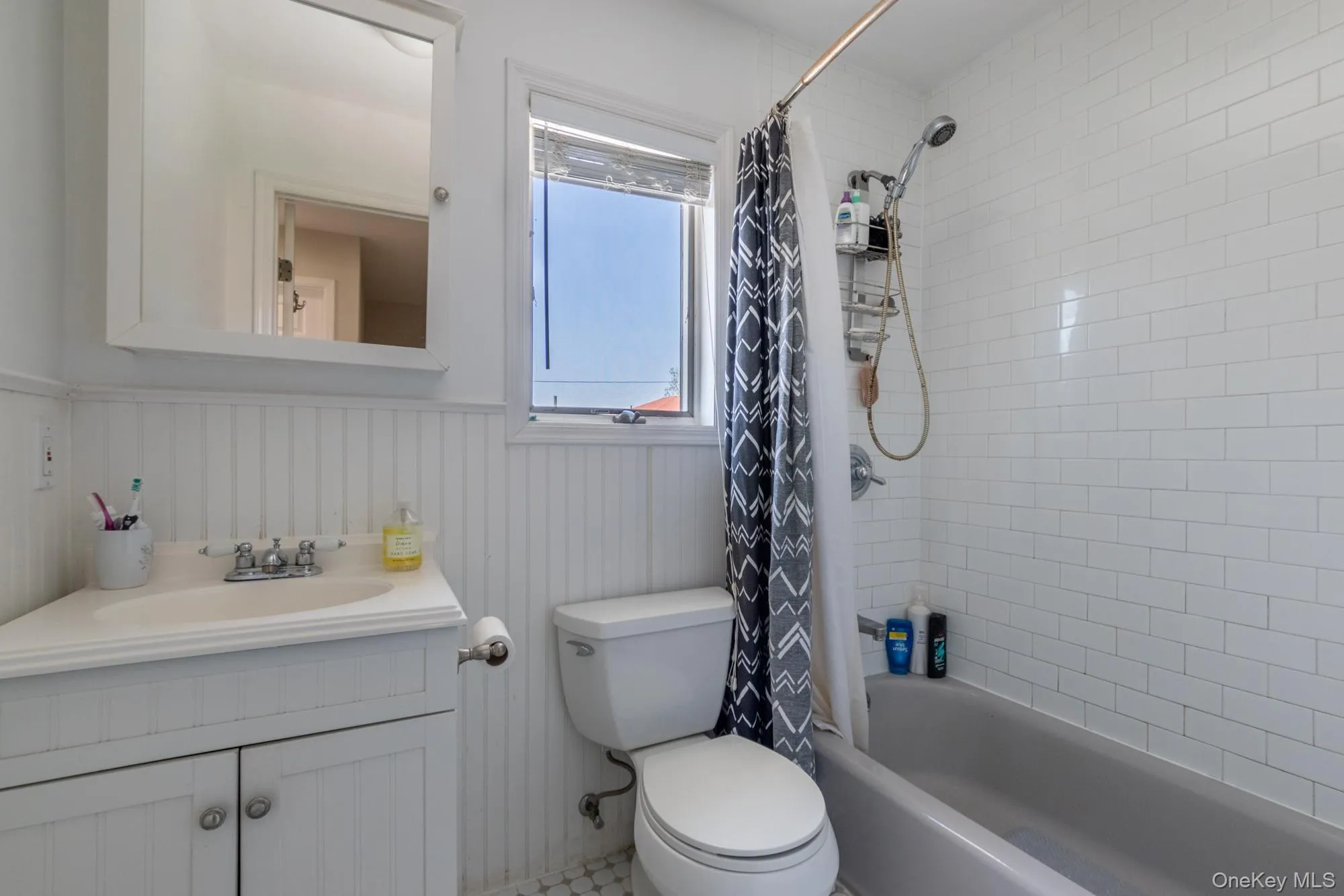 Bathroom featuring wainscoting, shower / tub combo, vanity, and a decorative wall Bathroom featuring wainscoting, shower / tub combo, vanity, and a decorative wall