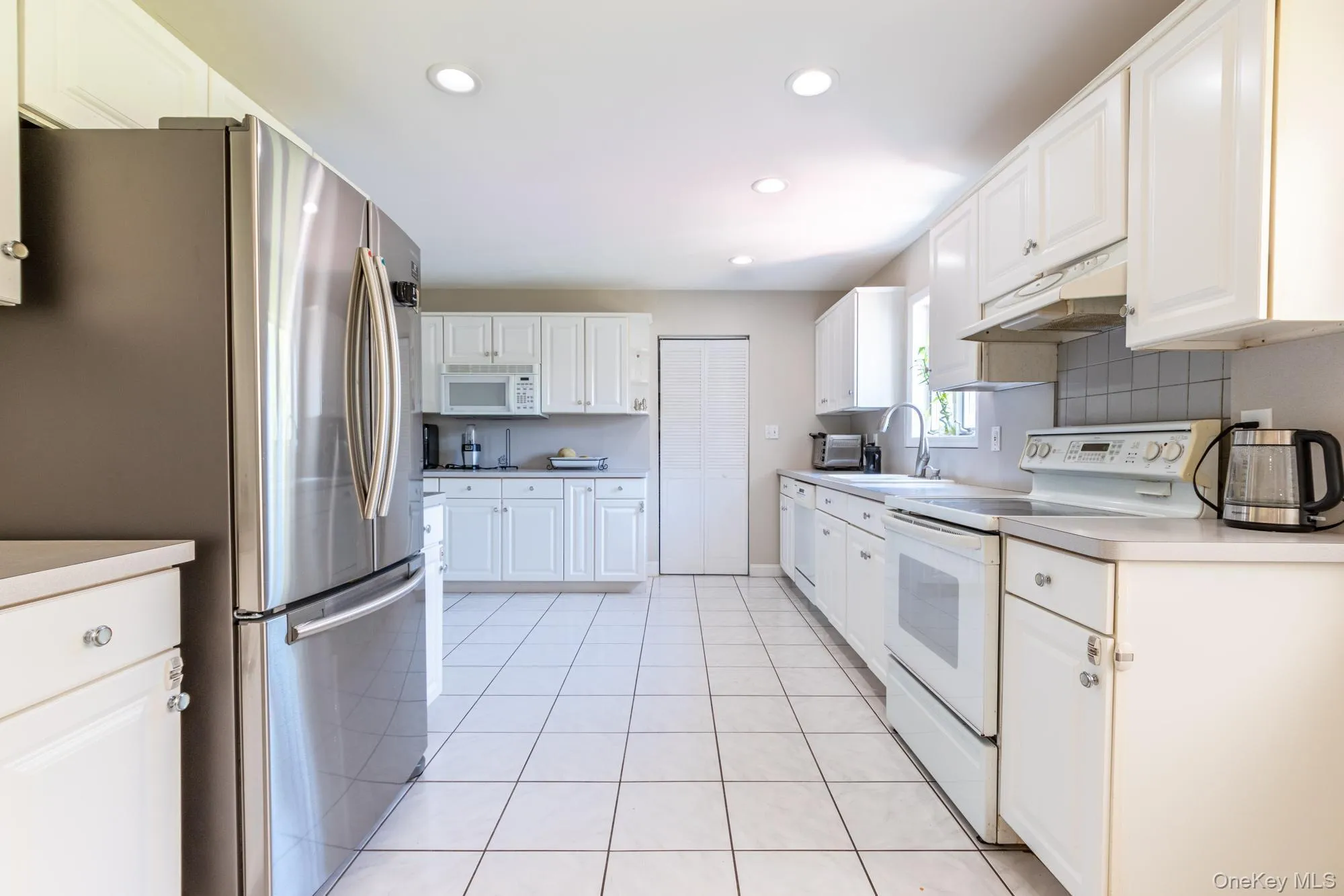 Kitchen featuring white appliances, white cabinets, recessed lighting, and light countertops Kitchen featuring white appliances, white cabinets, recessed lighting, and light countertops