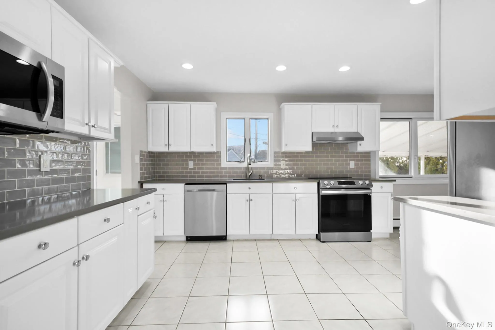 Kitchen featuring stainless steel appliances, white cabinets, recessed lighting, light tile patterned floors, and under cabinet range hood Kitchen featuring stainless steel appliances, white cabinets, recessed lighting, light tile patterned floors, and under cabinet range hood