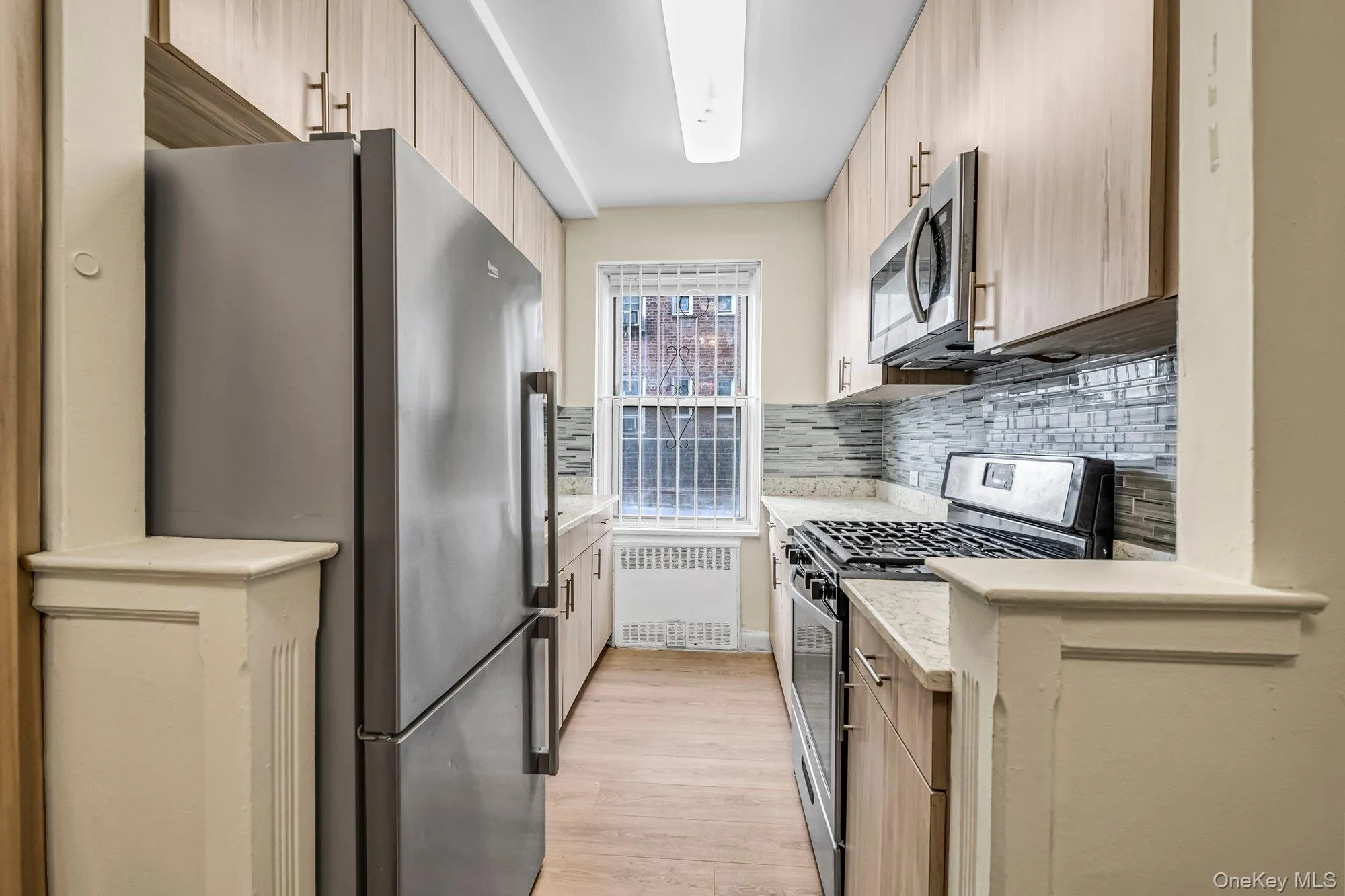 Kitchen with appliances with stainless steel finishes, radiator, light stone counters, tasteful backsplash, and light wood finished floors Kitchen with appliances with stainless steel finishes, radiator, light stone counters, tasteful backsplash, and light wood finished floors