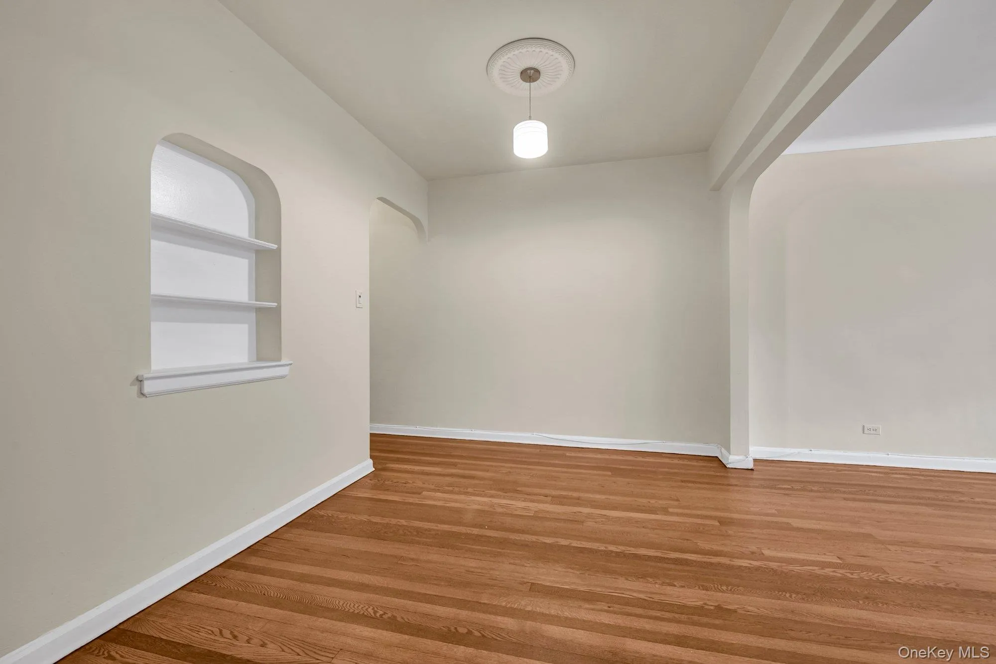 Unfurnished room featuring wood finished floors and arched walkways Unfurnished room featuring wood finished floors and arched walkways