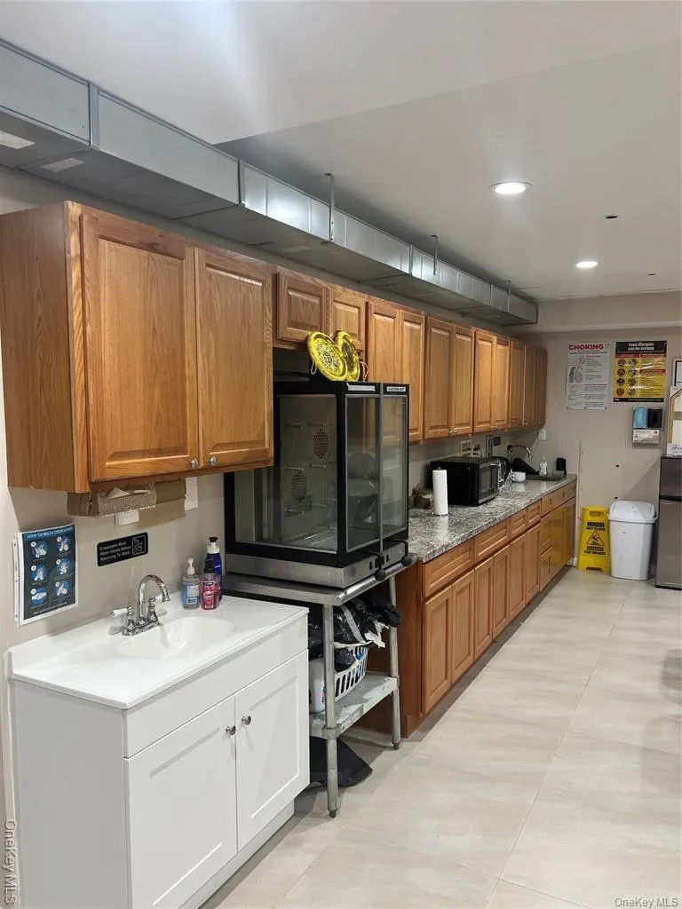 Kitchen with brown cabinets, light stone counters, recessed lighting, and black microwave Kitchen with brown cabinets, light stone counters, recessed lighting, and black microwave