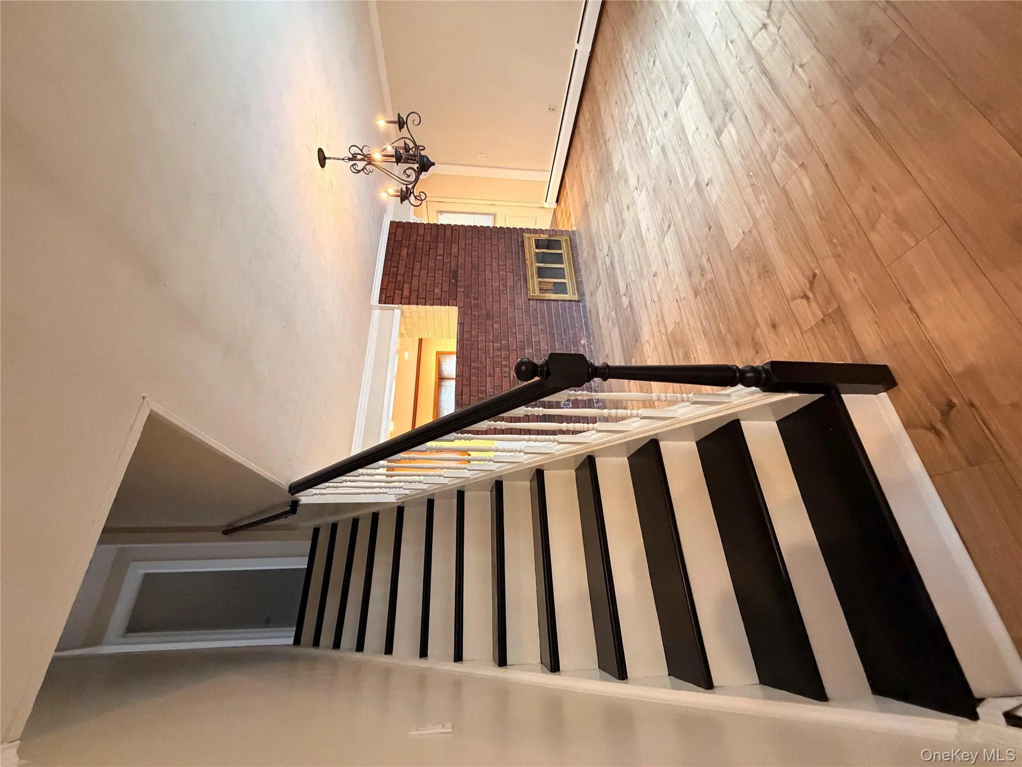Stairway featuring baseboard heating, wood-type flooring, a chandelier, crown molding, and a fireplace Stairway featuring baseboard heating, wood-type flooring, a chandelier, crown molding, and a fireplace