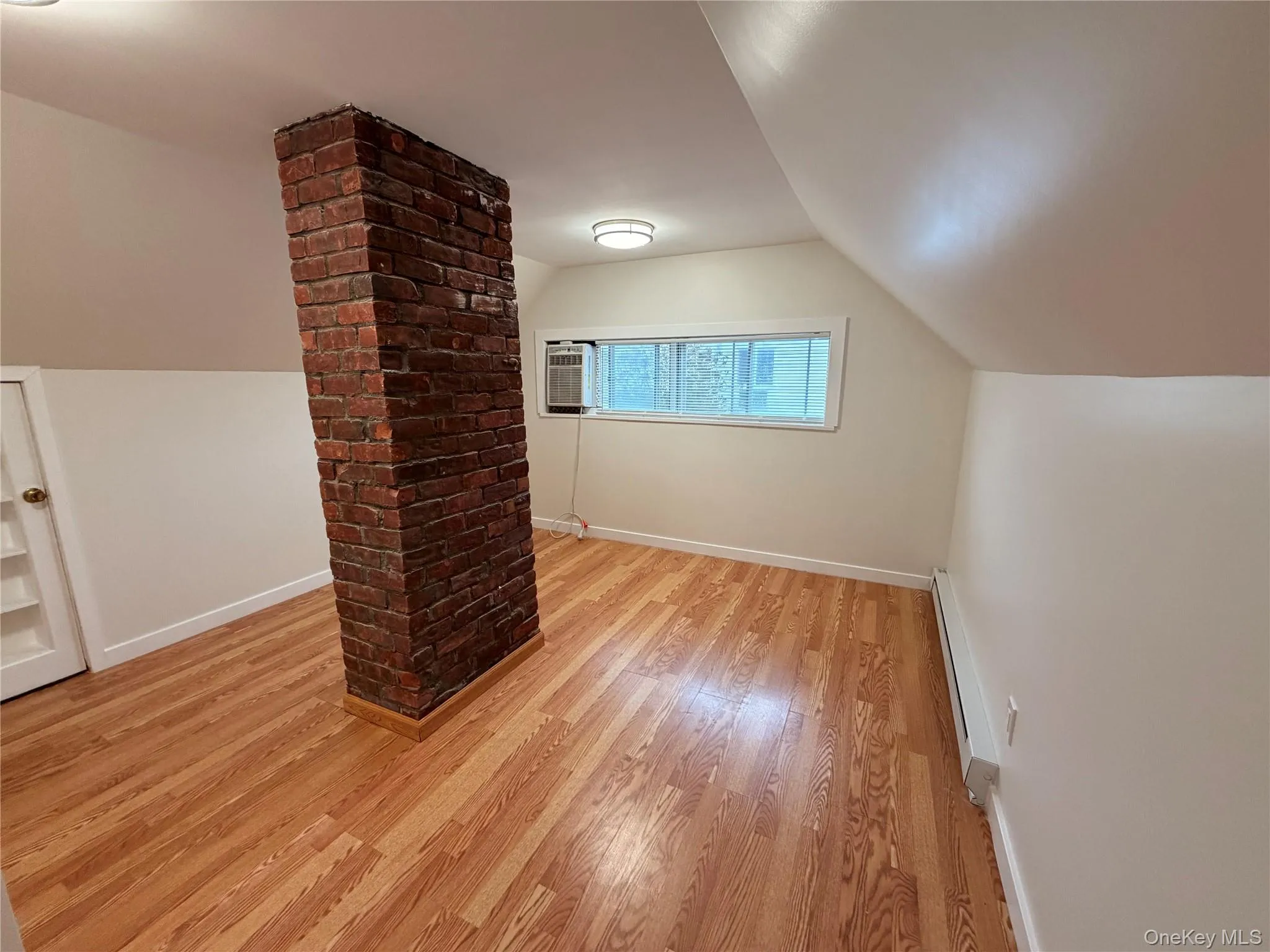 Additional living space with vaulted ceiling, light wood finished floors, and a baseboard heating unit Additional living space with vaulted ceiling, light wood finished floors, and a baseboard heating unit