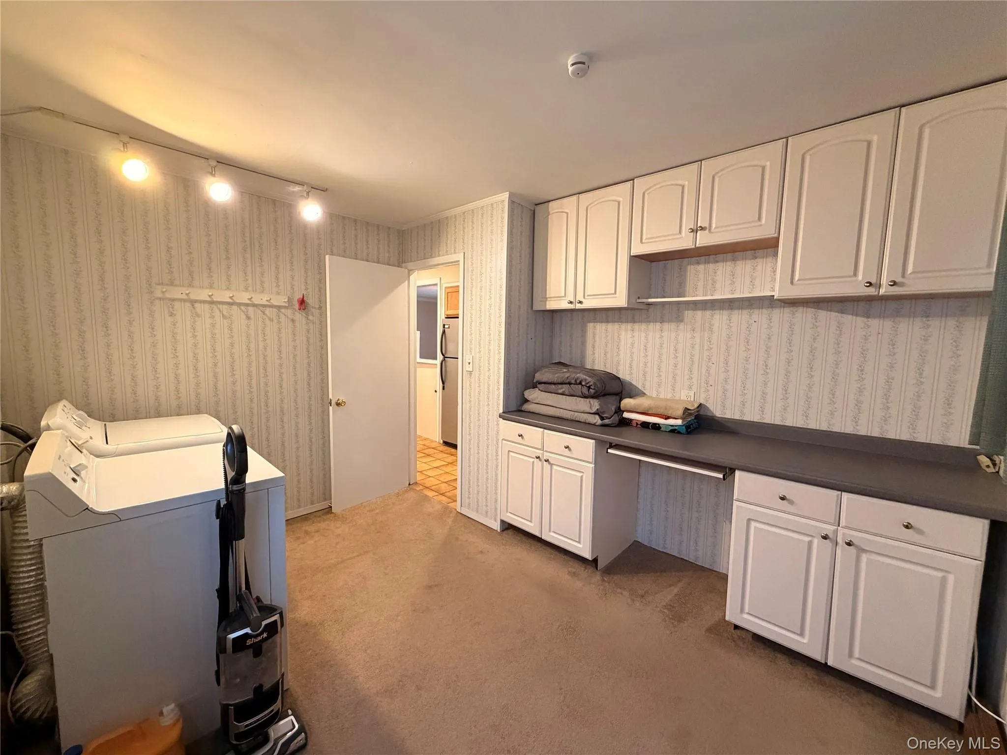 Kitchen with built in desk, dark countertops, washer and dryer, light colored carpet, and white cabinetry Kitchen with built in desk, dark countertops, washer and dryer, light colored carpet, and white cabinetry