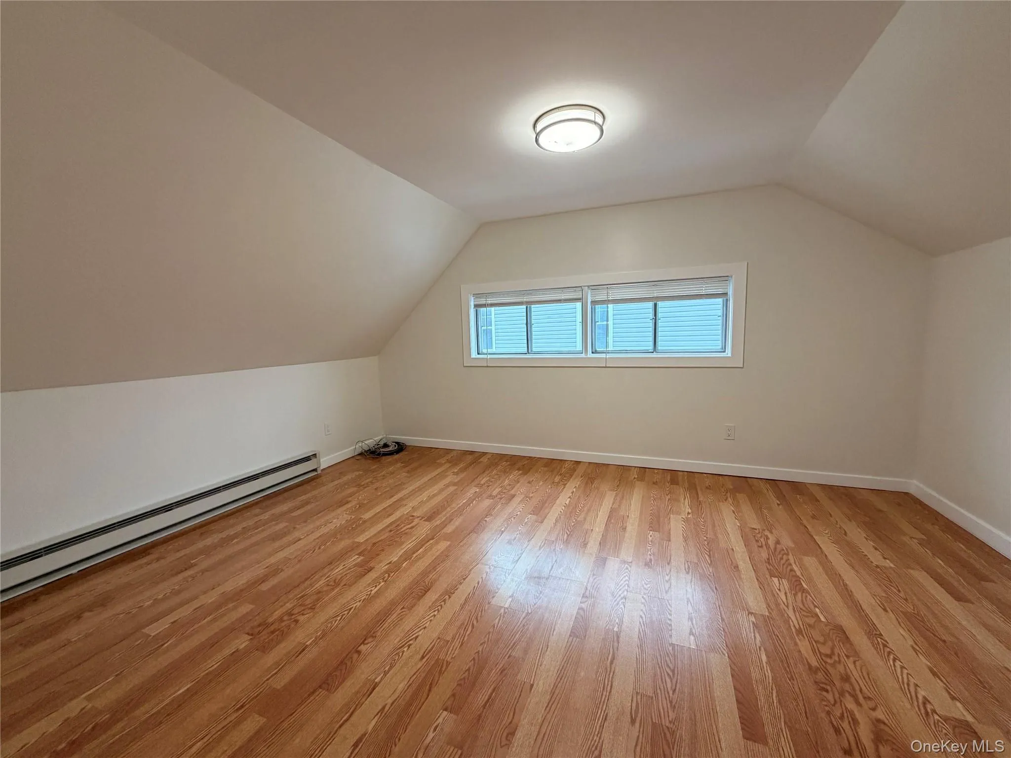 Additional living space featuring a baseboard radiator, vaulted ceiling, and light wood-style flooring Additional living space featuring a baseboard radiator, vaulted ceiling, and light wood-style flooring