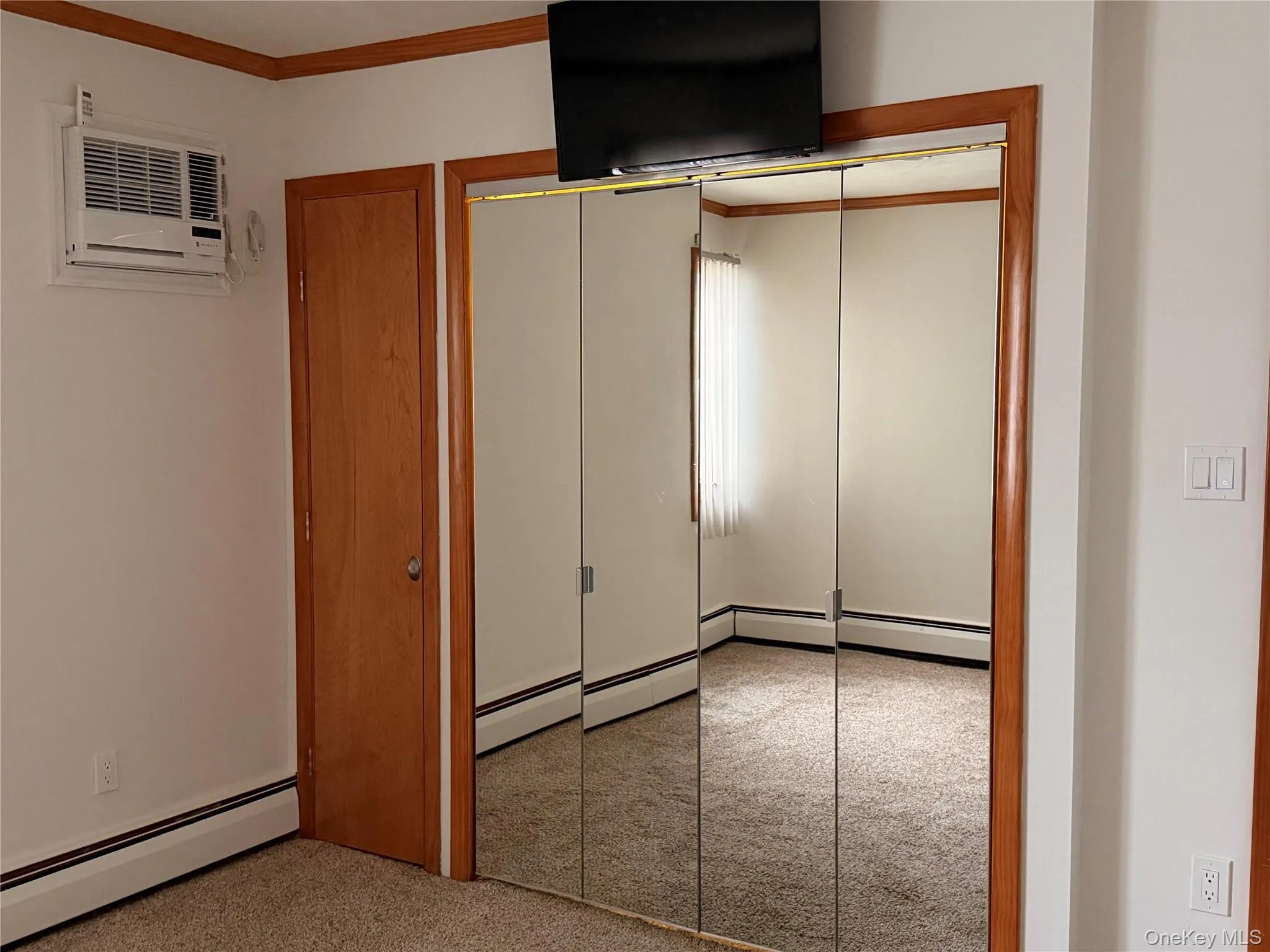 Unfurnished bedroom featuring baseboard heating, a closet, ornamental molding, a wall mounted AC, and carpet Unfurnished bedroom featuring baseboard heating, a closet, ornamental molding, a wall mounted AC, and carpet