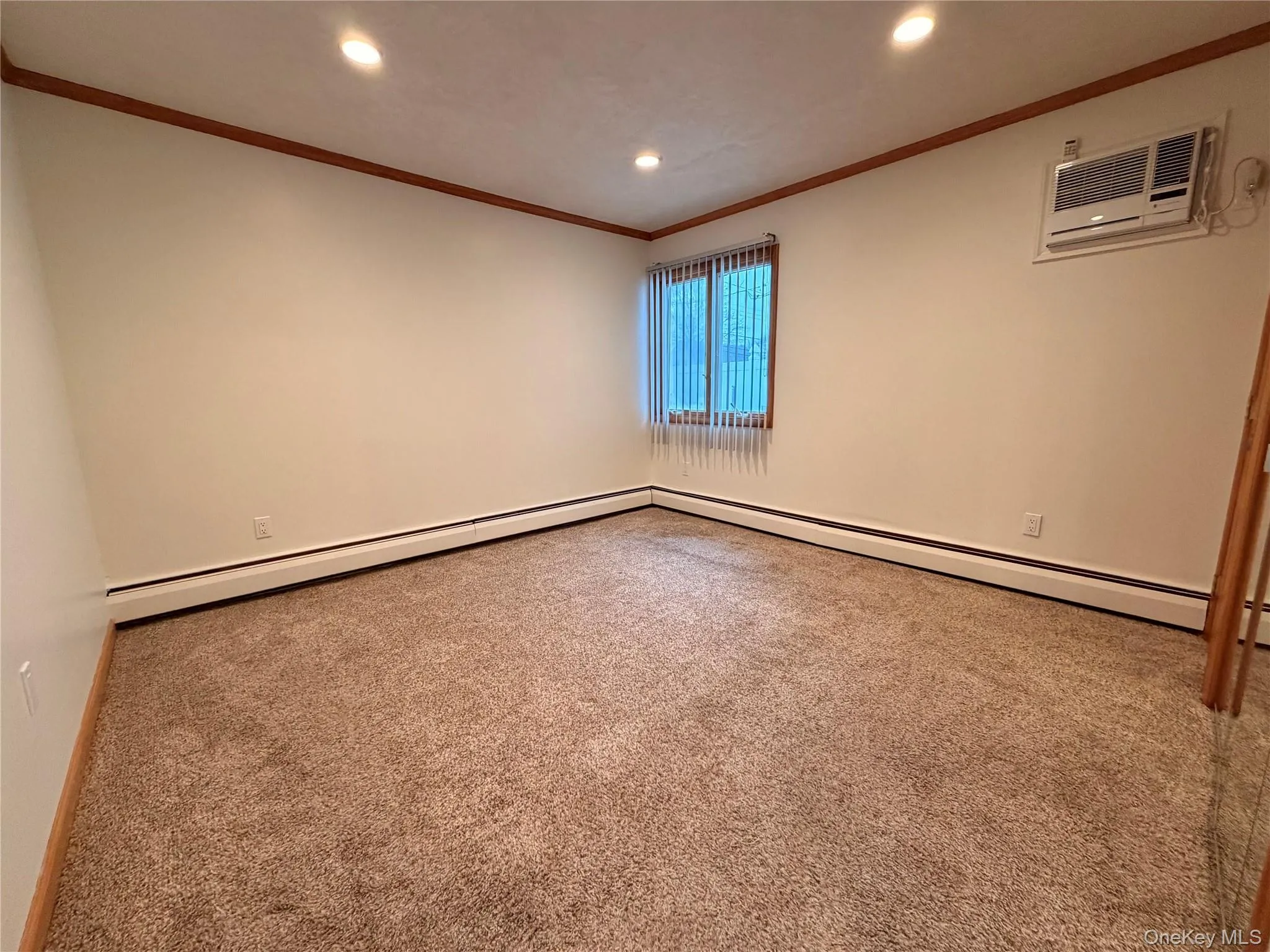 Carpeted empty room featuring recessed lighting, baseboard heating, crown molding, and a wall mounted AC Carpeted empty room featuring recessed lighting, baseboard heating, crown molding, and a wall mounted AC