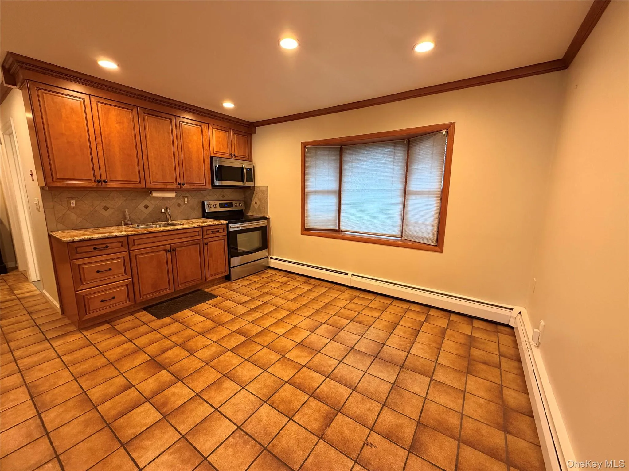 Kitchen with stainless steel appliances, brown cabinets, crown molding, light stone countertops, and recessed lighting Kitchen with stainless steel appliances, brown cabinets, crown molding, light stone countertops, and recessed lighting