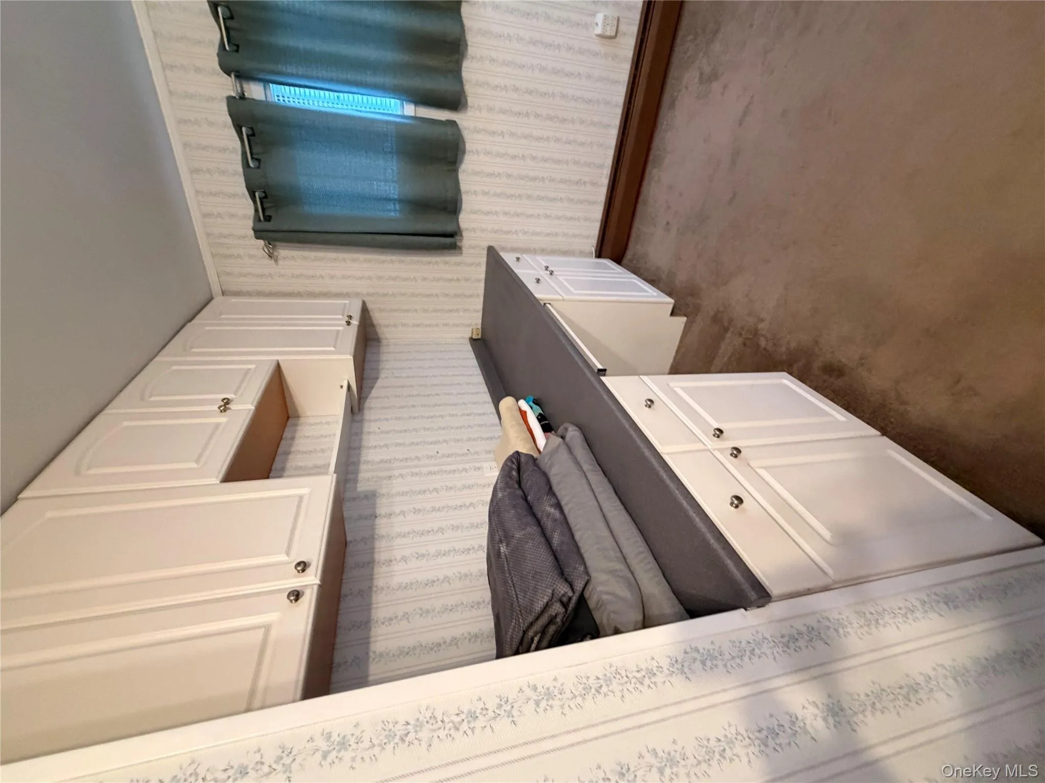 Kitchen featuring built in desk, white cabinetry, dark countertops, dark colored carpet, and wallpapered walls Kitchen featuring built in desk, white cabinetry, dark countertops, dark colored carpet, and wallpapered walls