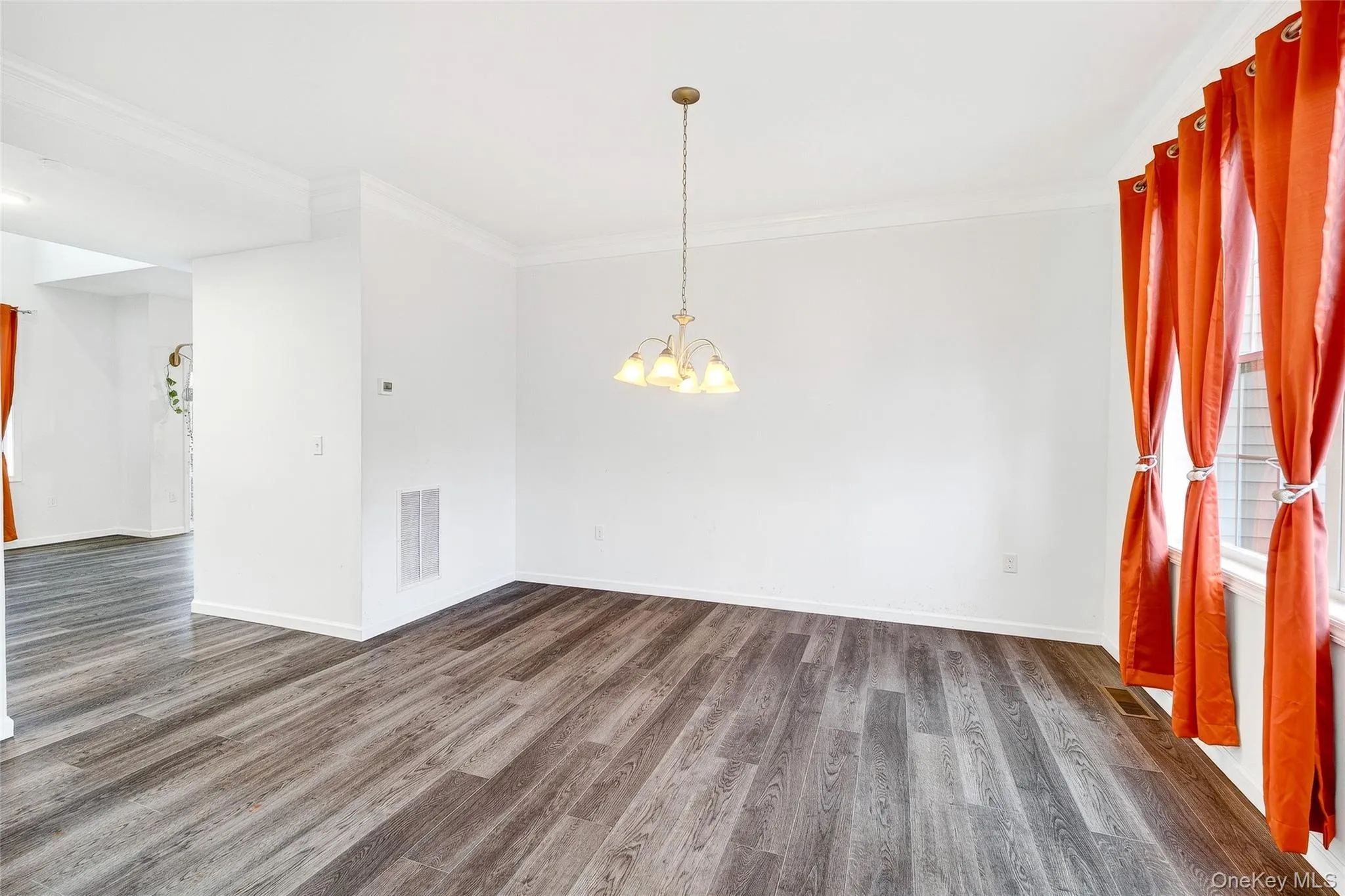 Unfurnished room featuring dark wood-style flooring, ornamental molding, and a chandelier Unfurnished room featuring dark wood-style flooring, ornamental molding, and a chandelier