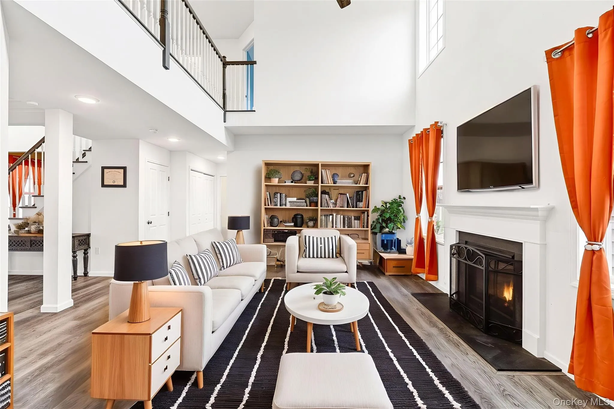 Living room featuring a high ceiling, a fireplace with flush hearth, wood finished floors, and stairway Living room featuring a high ceiling, a fireplace with flush hearth, wood finished floors, and stairway