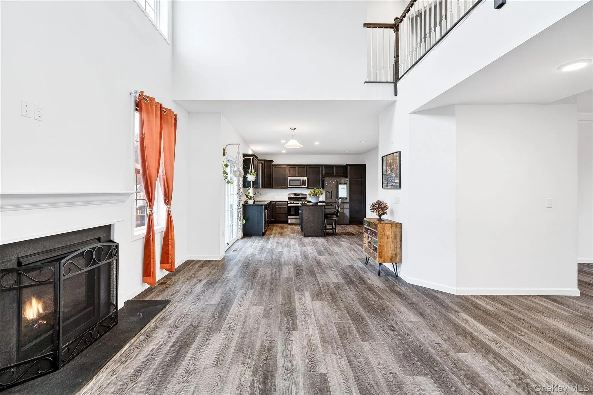 Living room with a lit fireplace, light wood finished floors, a high ceiling, and recessed lighting Living room with a lit fireplace, light wood finished floors, a high ceiling, and recessed lighting