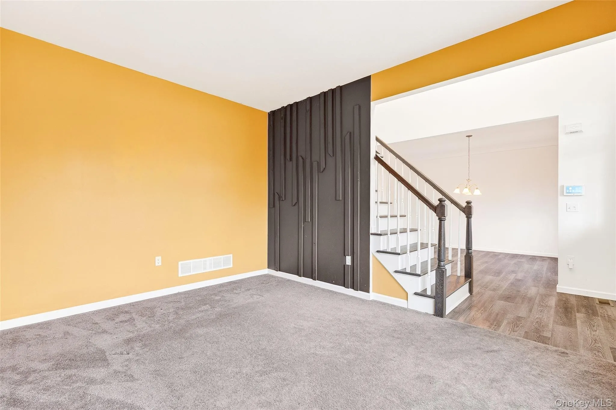 Carpeted empty room with stairway, a chandelier, and wood finished floors Carpeted empty room with stairway, a chandelier, and wood finished floors