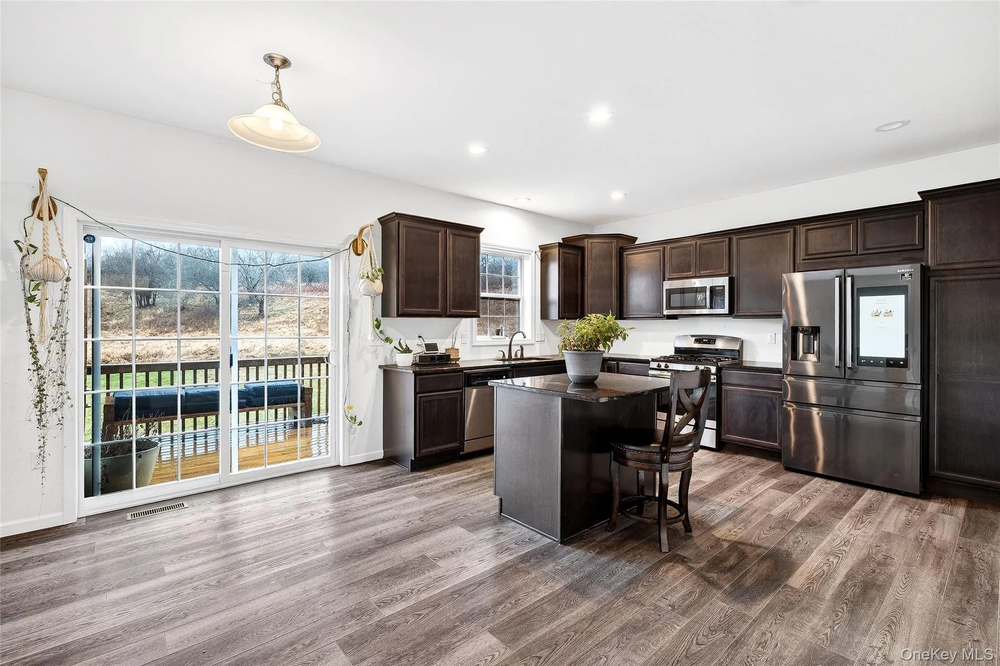 Kitchen featuring stainless steel appliances, dark brown cabinetry, a center island, a kitchen bar, and dark wood-style floors Kitchen featuring stainless steel appliances, dark brown cabinetry, a center island, a kitchen bar, and dark wood-style floors