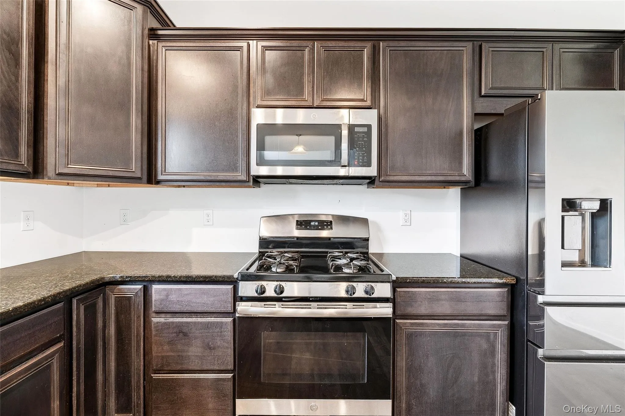 Kitchen with stainless steel appliances, dark brown cabinetry, and dark stone countertops Kitchen with stainless steel appliances, dark brown cabinetry, and dark stone countertops