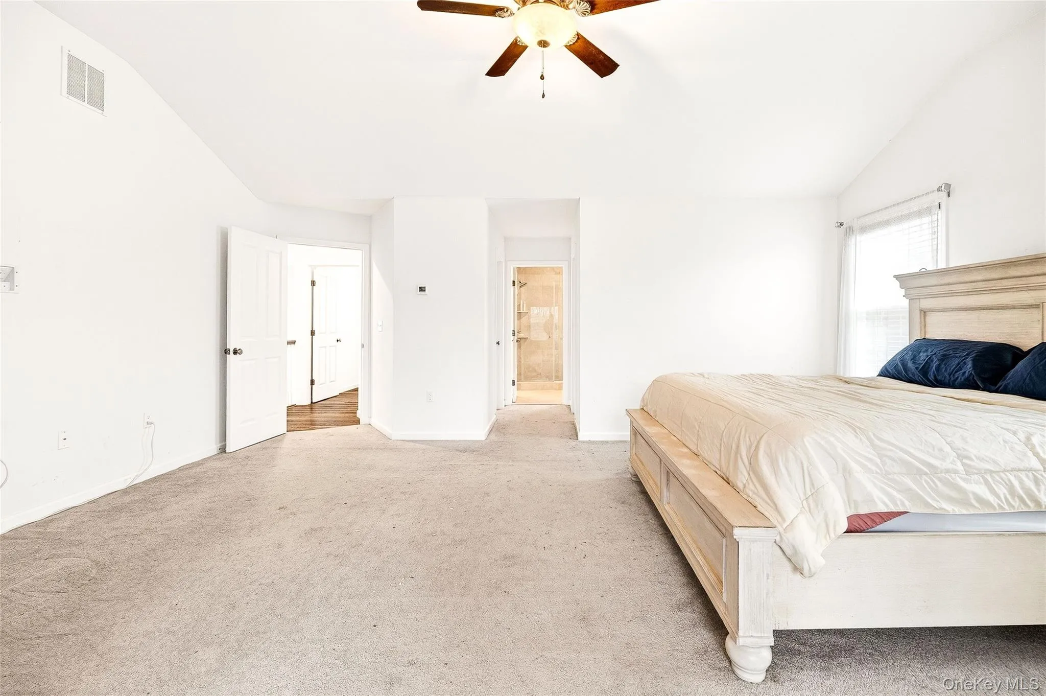Carpeted bedroom with vaulted ceiling, a ceiling fan, and ensuite bathroom Carpeted bedroom with vaulted ceiling, a ceiling fan, and ensuite bathroom