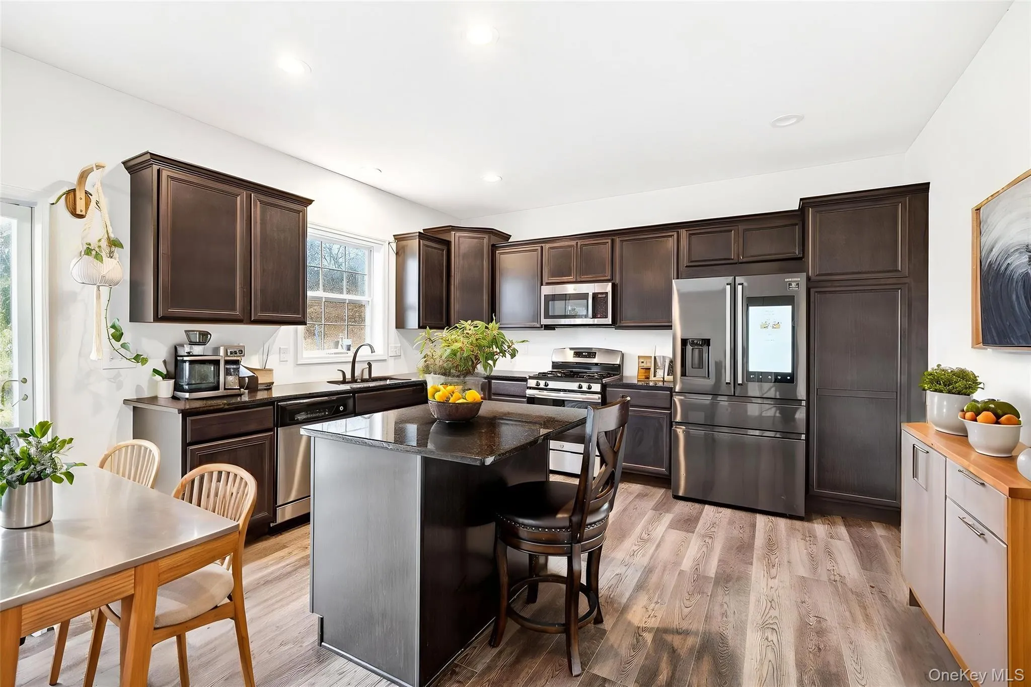 Kitchen featuring dark brown cabinets, stainless steel appliances, light wood-type flooring, a kitchen bar, and recessed lighting Kitchen featuring dark brown cabinets, stainless steel appliances, light wood-type flooring, a kitchen bar, and recessed lighting