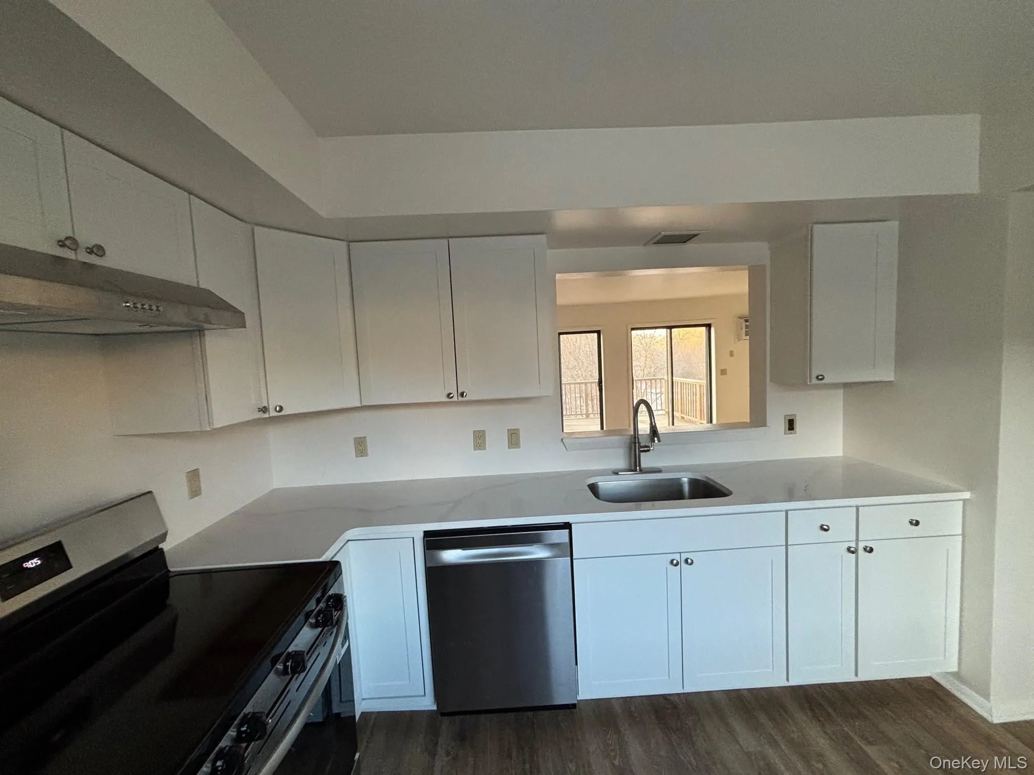 Kitchen with stainless steel appliances, white cabinetry, under cabinet range hood, dark wood-type flooring, and light stone countertops Kitchen with stainless steel appliances, white cabinetry, under cabinet range hood, dark wood-type flooring, and light stone countertops