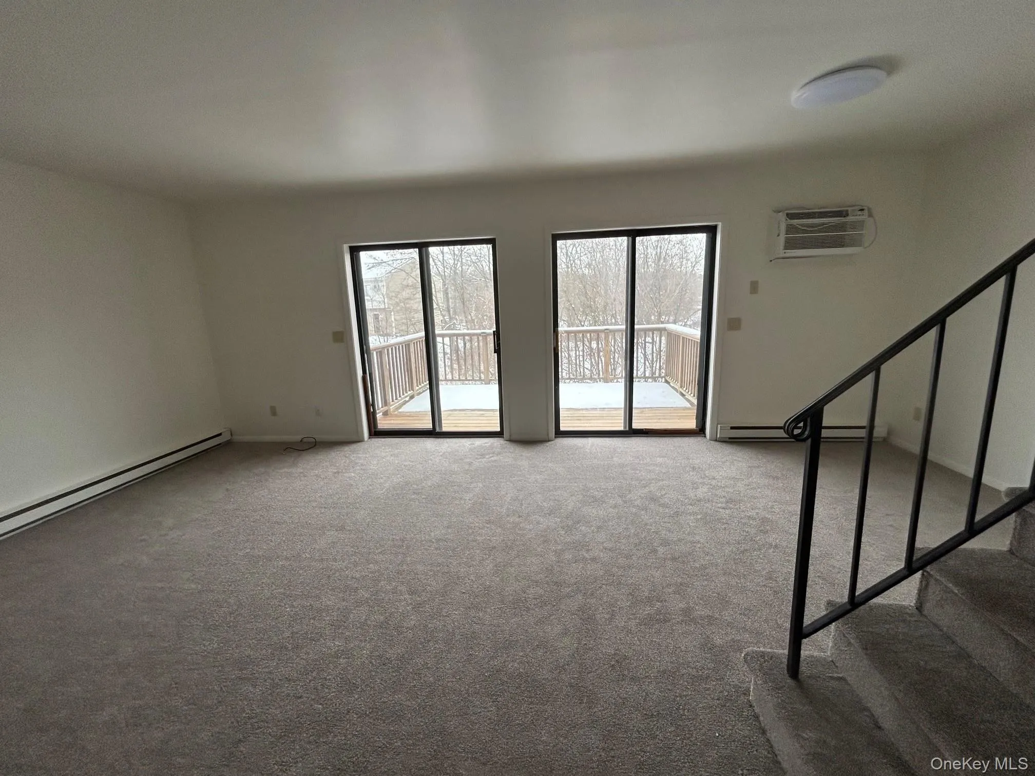 Unfurnished living room with light colored carpet, stairs, a wall unit AC, and a baseboard heating unit Unfurnished living room with light colored carpet, stairs, a wall unit AC, and a baseboard heating unit