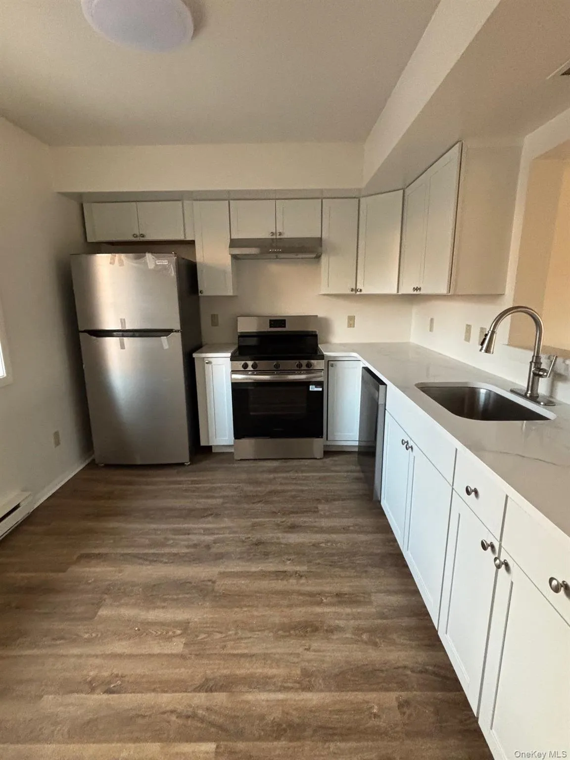 Kitchen with appliances with stainless steel finishes, white cabinets, dark wood-type flooring, and light stone counters Kitchen with appliances with stainless steel finishes, white cabinets, dark wood-type flooring, and light stone counters