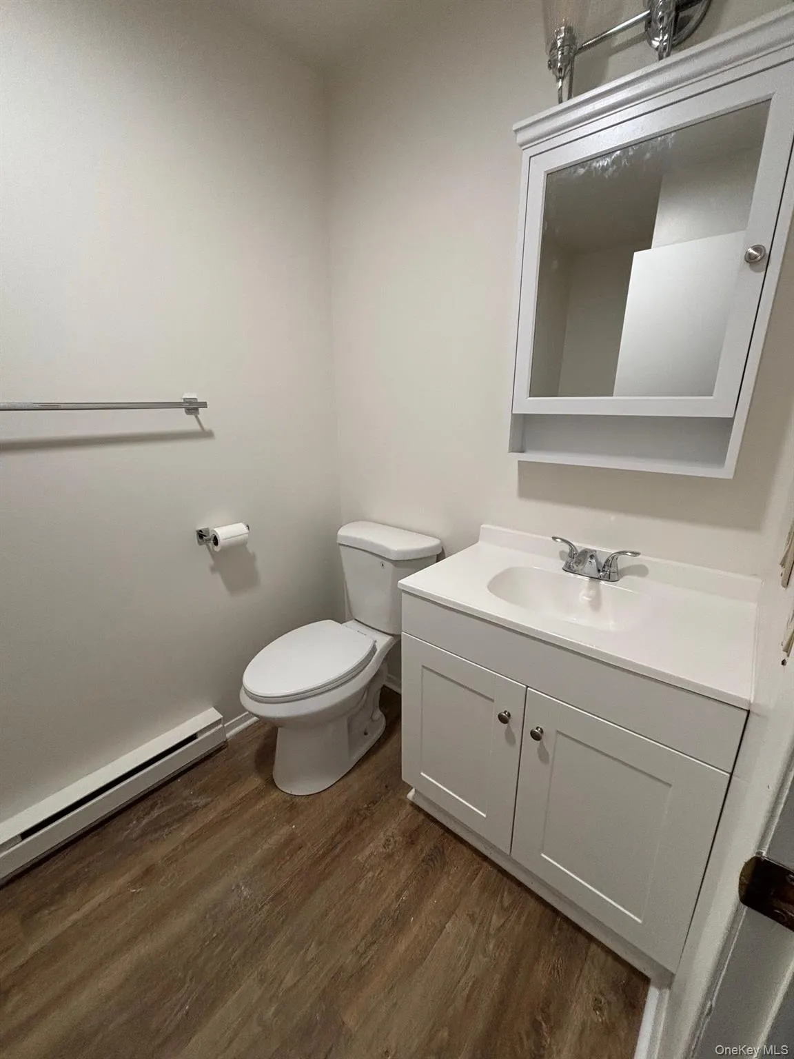 Half bathroom with a baseboard heating unit, vanity, and dark wood-style flooring Half bathroom with a baseboard heating unit, vanity, and dark wood-style flooring