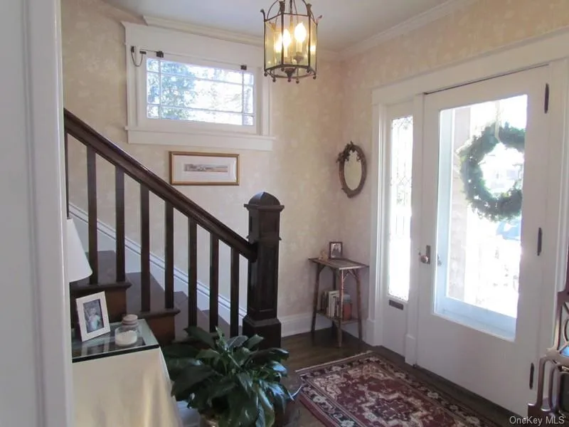 Foyer entrance featuring dark wood-type flooring, an inviting chandelier, ornamental molding, and a healthy amount of sunlight Foyer entrance featuring dark wood-type flooring, an inviting chandelier, ornamental molding, and a healthy amount of sunlight
