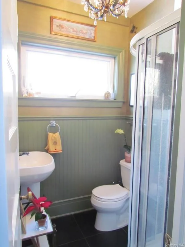 Bathroom featuring toilet, wooden walls, a notable chandelier, tile patterned flooring, and an enclosed shower Bathroom featuring toilet, wooden walls, a notable chandelier, tile patterned flooring, and an enclosed shower