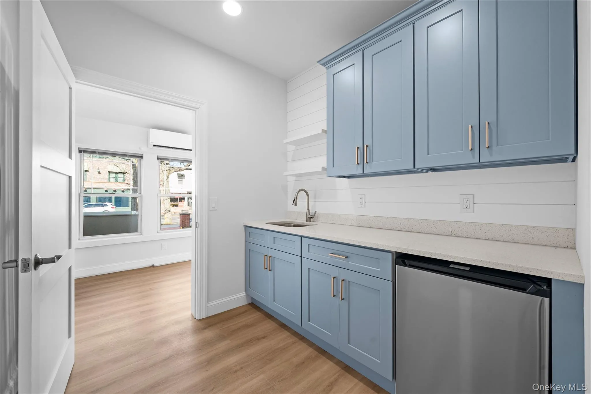 Kitchen featuring blue cabinets, stainless steel dishwasher, light stone counters, open shelves, and light wood finished floors Kitchen featuring blue cabinets, stainless steel dishwasher, light stone counters, open shelves, and light wood finished floors