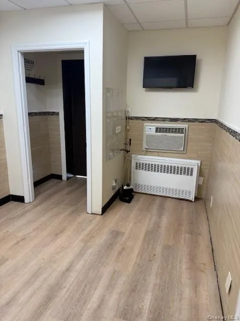 Living area featuring a drop ceiling, radiator heating unit, light wood-type flooring, tile walls, and a wainscoted wall Living area featuring a drop ceiling, radiator heating unit, light wood-type flooring, tile walls, and a wainscoted wall