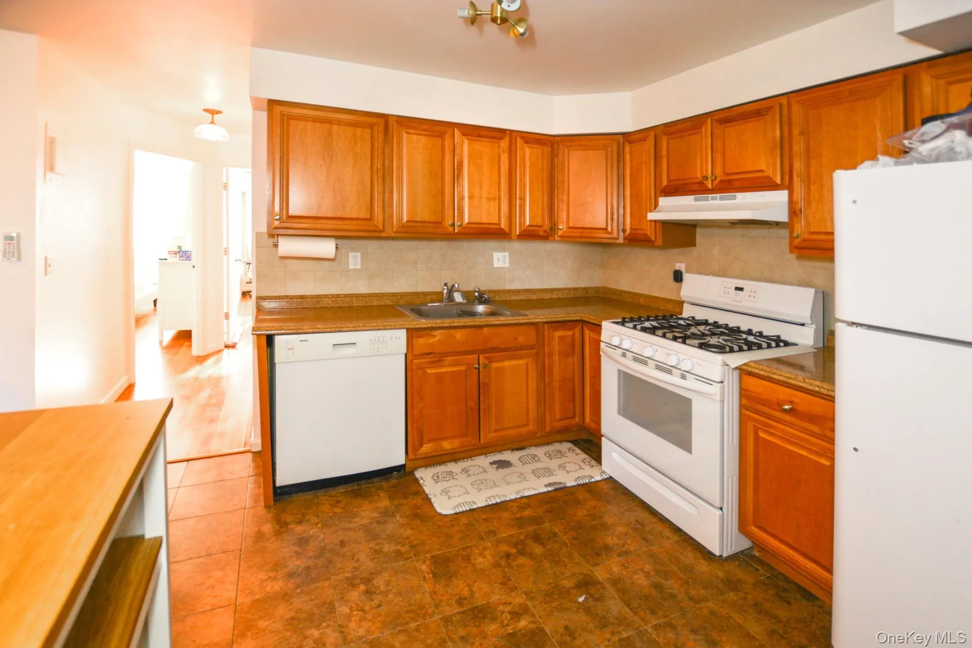 Kitchen with white appliances, brown cabinets, under cabinet range hood, and tasteful backsplash Kitchen with white appliances, brown cabinets, under cabinet range hood, and tasteful backsplash
