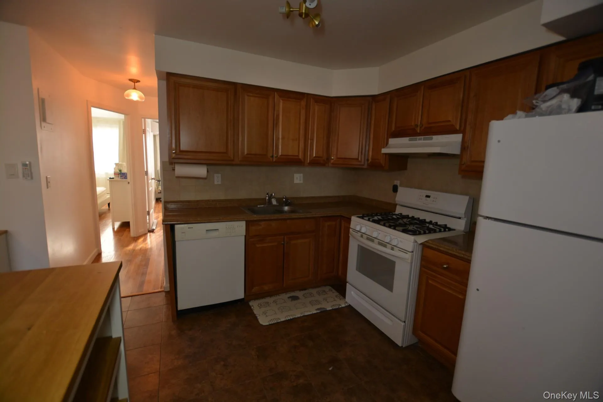Kitchen with white appliances, brown cabinetry, and under cabinet range hood Kitchen with white appliances, brown cabinetry, and under cabinet range hood