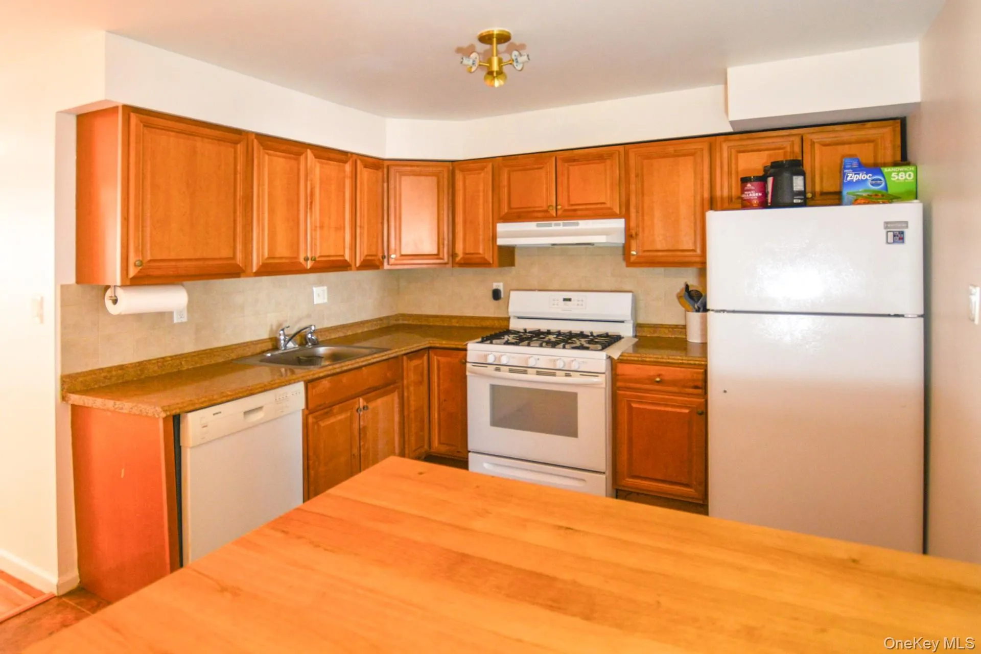 Kitchen with white appliances, brown cabinets, decorative backsplash, and under cabinet range hood Kitchen with white appliances, brown cabinets, decorative backsplash, and under cabinet range hood