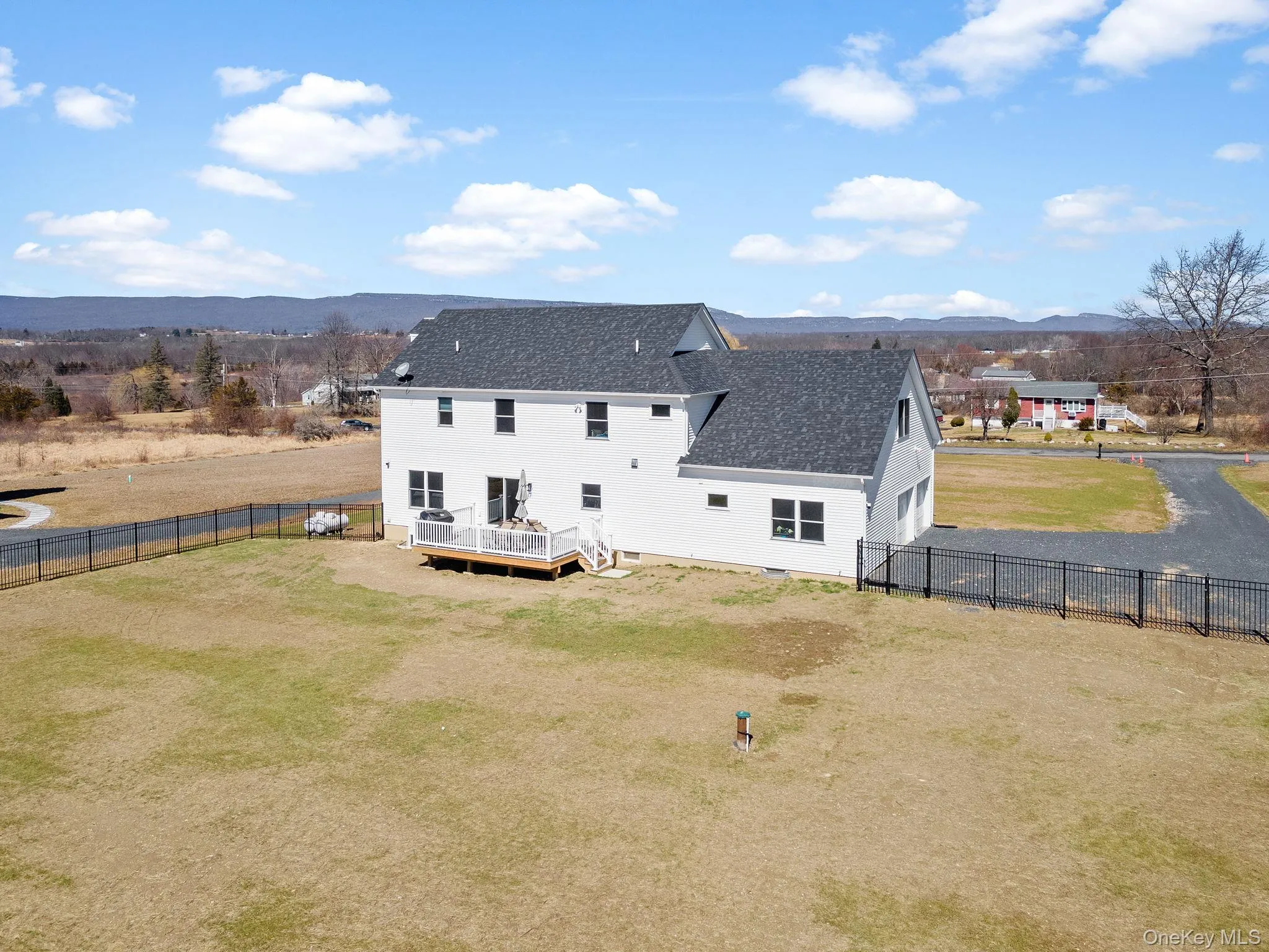 Back of house featuring a deck with mountain view, a fenced backyard, roof with shingles, driveway, and a garage Back of house featuring a deck with mountain view, a fenced backyard, roof with shingles, driveway, and a garage