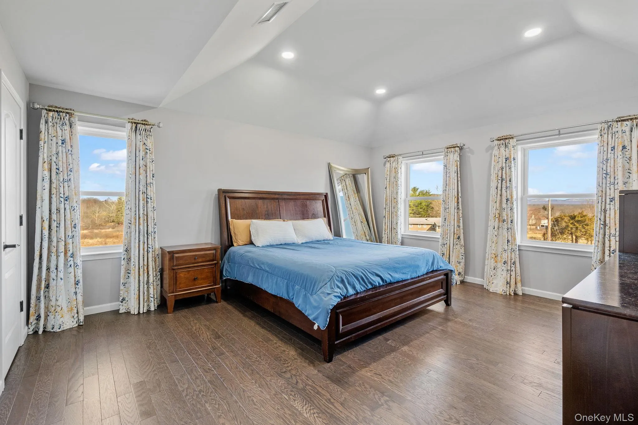 Bedroom with dark wood finished floors, vaulted ceiling, multiple windows, and recessed lighting Bedroom with dark wood finished floors, vaulted ceiling, multiple windows, and recessed lighting