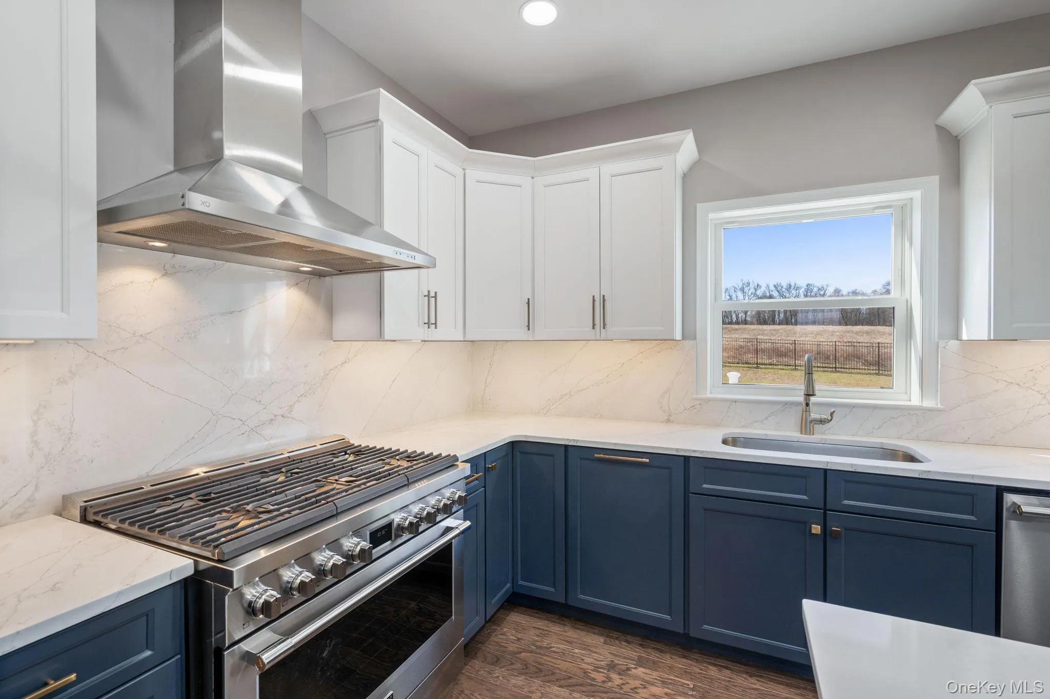 Kitchen featuring appliances with stainless steel finishes, wall chimney exhaust hood, light stone countertops, white cabinets, and blue cabinetry Kitchen featuring appliances with stainless steel finishes, wall chimney exhaust hood, light stone countertops, white cabinets, and blue cabinetry
