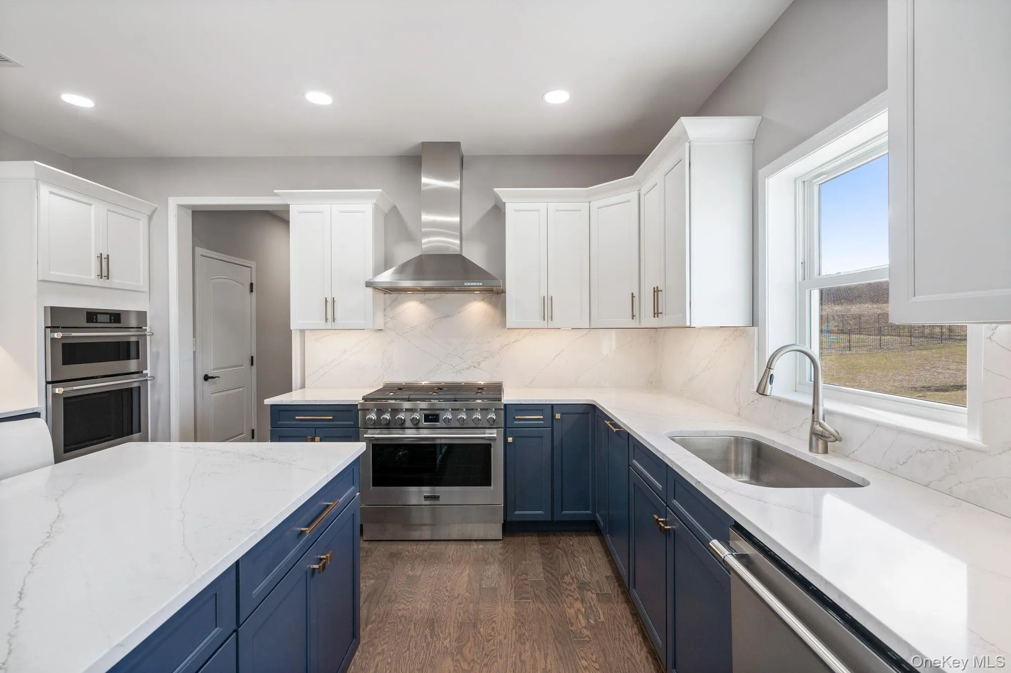 Kitchen featuring blue cabinets, light stone counters, stainless steel appliances, wall chimney range hood, and white cabinetry Kitchen featuring blue cabinets, light stone counters, stainless steel appliances, wall chimney range hood, and white cabinetry