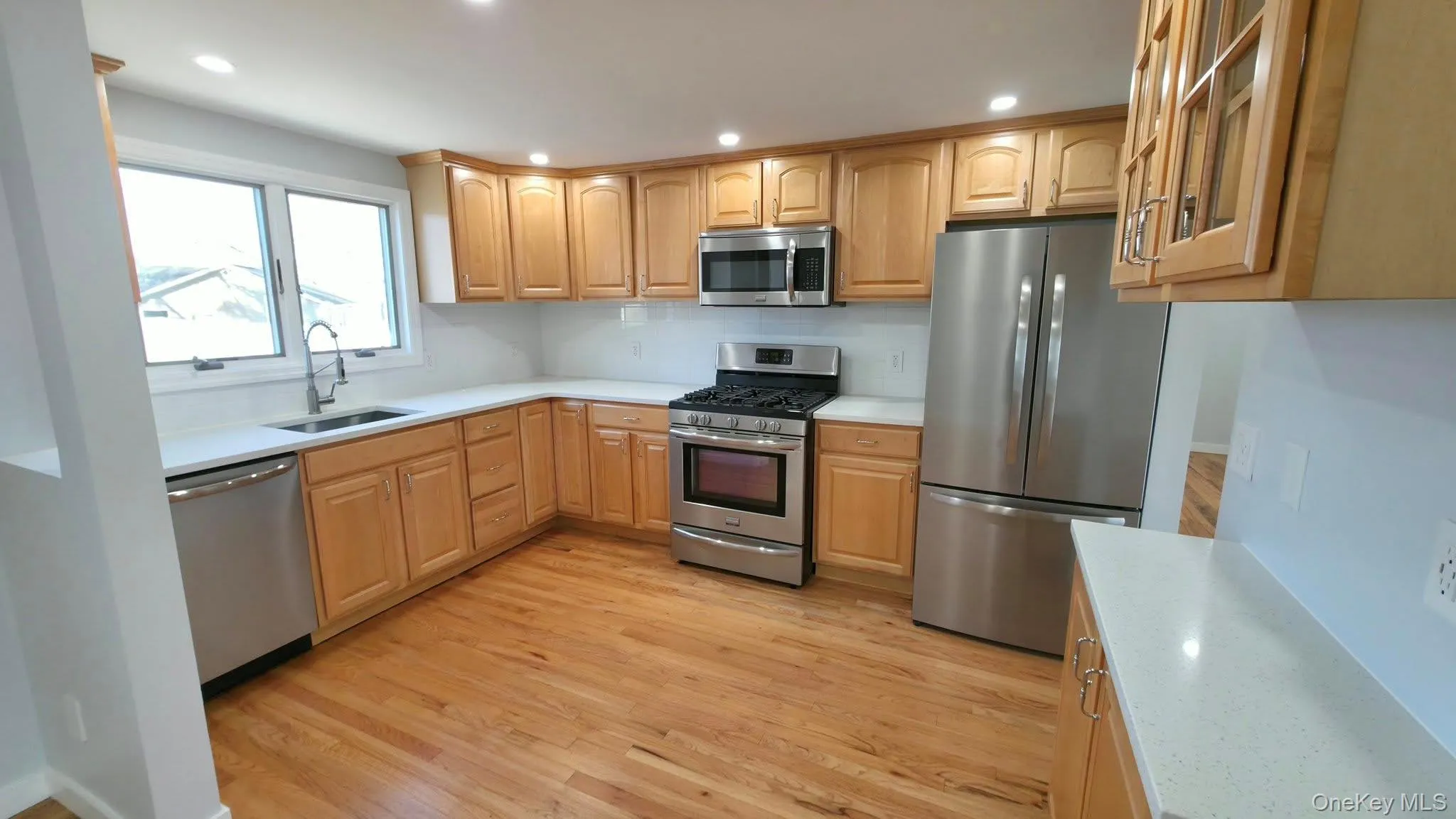 Kitchen featuring stainless steel appliances, glass insert cabinets, light brown cabinets, light wood finished floors, and recessed lighting Kitchen featuring stainless steel appliances, glass insert cabinets, light brown cabinets, light wood finished floors, and recessed lighting