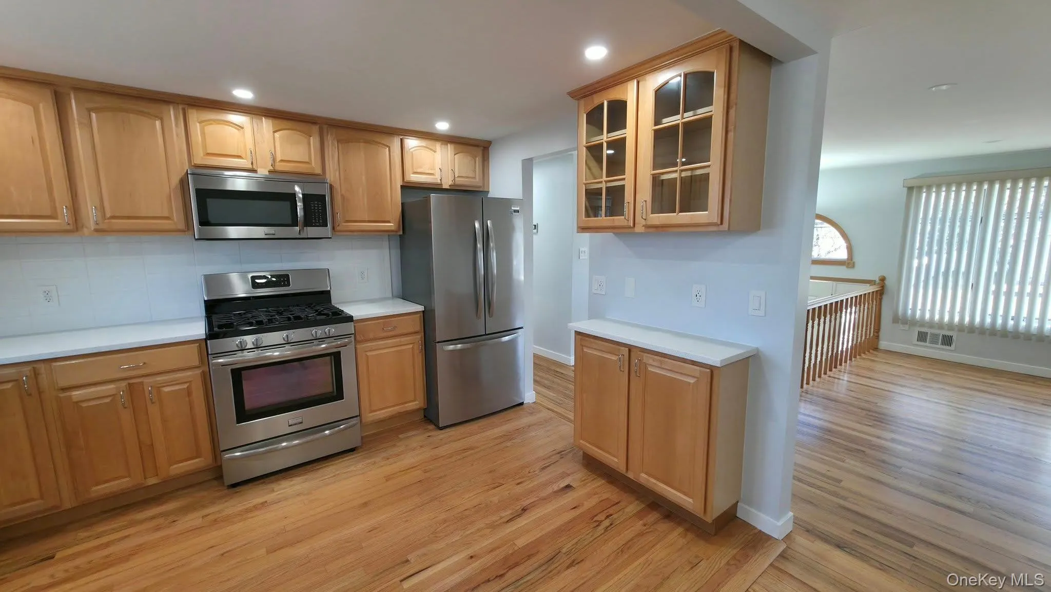 Kitchen featuring stainless steel appliances, glass insert cabinets, tasteful backsplash, light countertops, and light wood-style flooring Kitchen featuring stainless steel appliances, glass insert cabinets, tasteful backsplash, light countertops, and light wood-style flooring