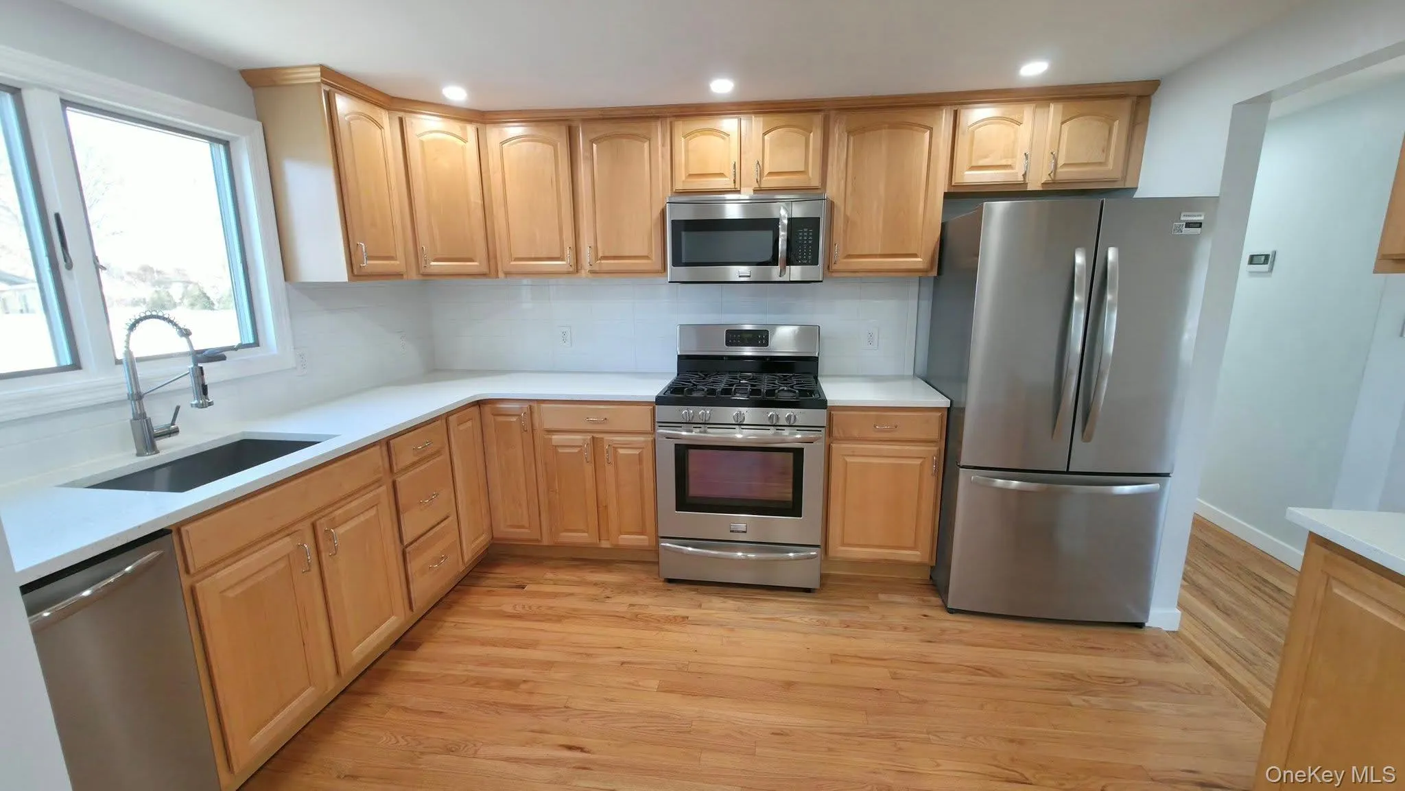 Kitchen with appliances with stainless steel finishes, tasteful backsplash, light wood-type flooring, light brown cabinets, and recessed lighting Kitchen with appliances with stainless steel finishes, tasteful backsplash, light wood-type flooring, light brown cabinets, and recessed lighting