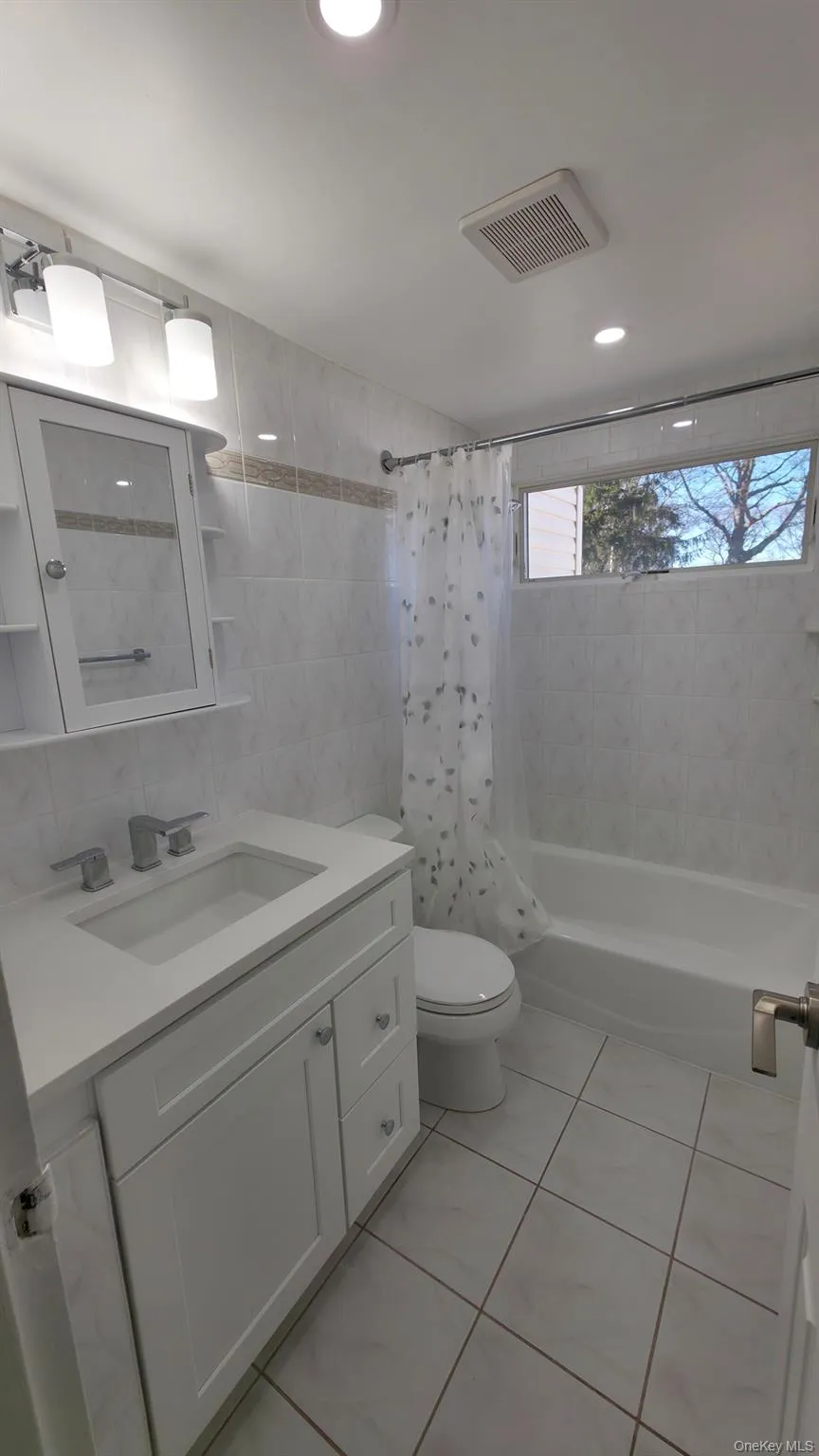 Bathroom featuring tile walls, shower / bathtub combination with curtain, vanity, light tile patterned floors, and recessed lighting Bathroom featuring tile walls, shower / bathtub combination with curtain, vanity, light tile patterned floors, and recessed lighting
