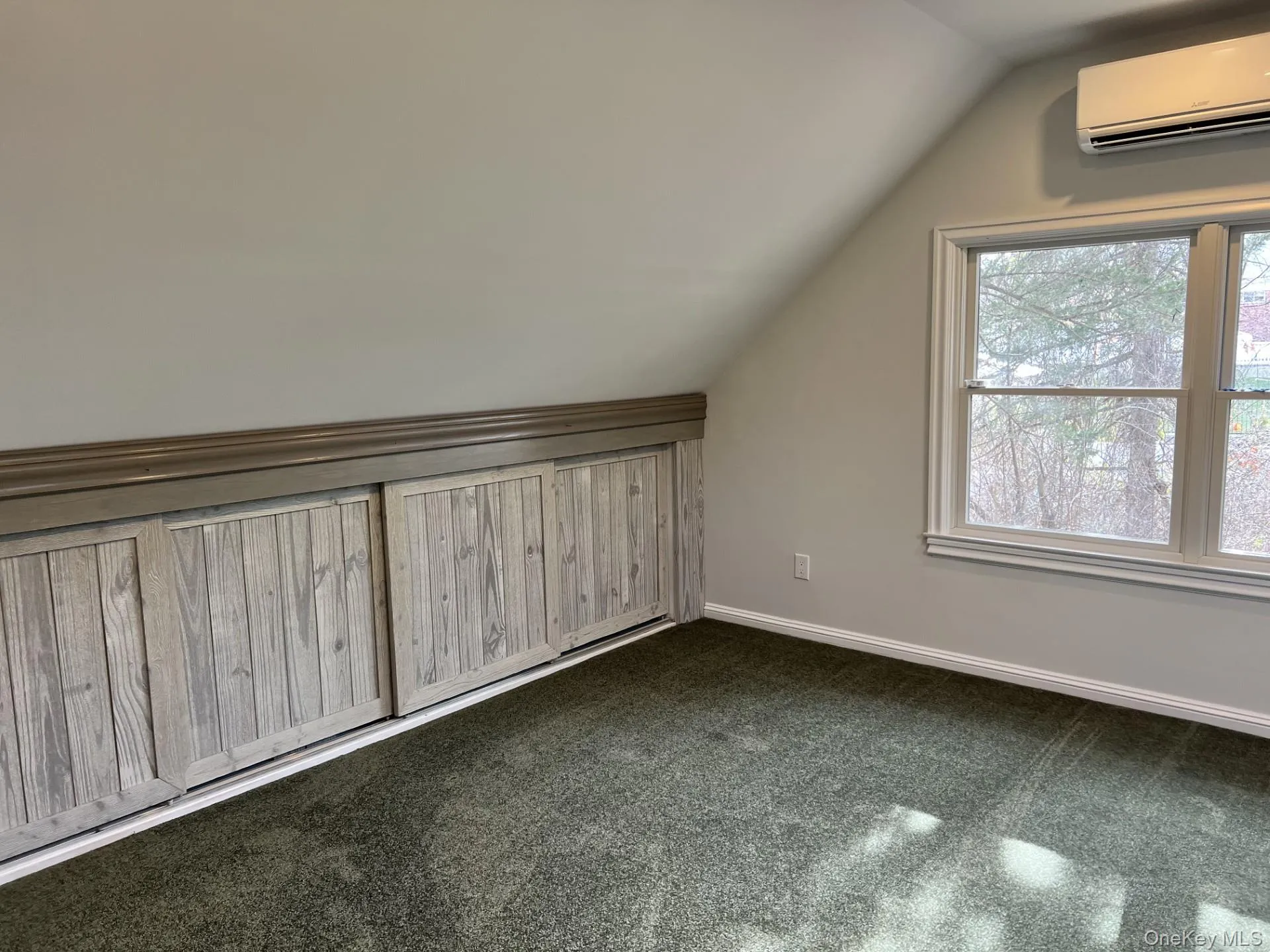 Additional living space featuring lofted ceiling, an AC wall unit, and dark carpet Additional living space featuring lofted ceiling, an AC wall unit, and dark carpet
