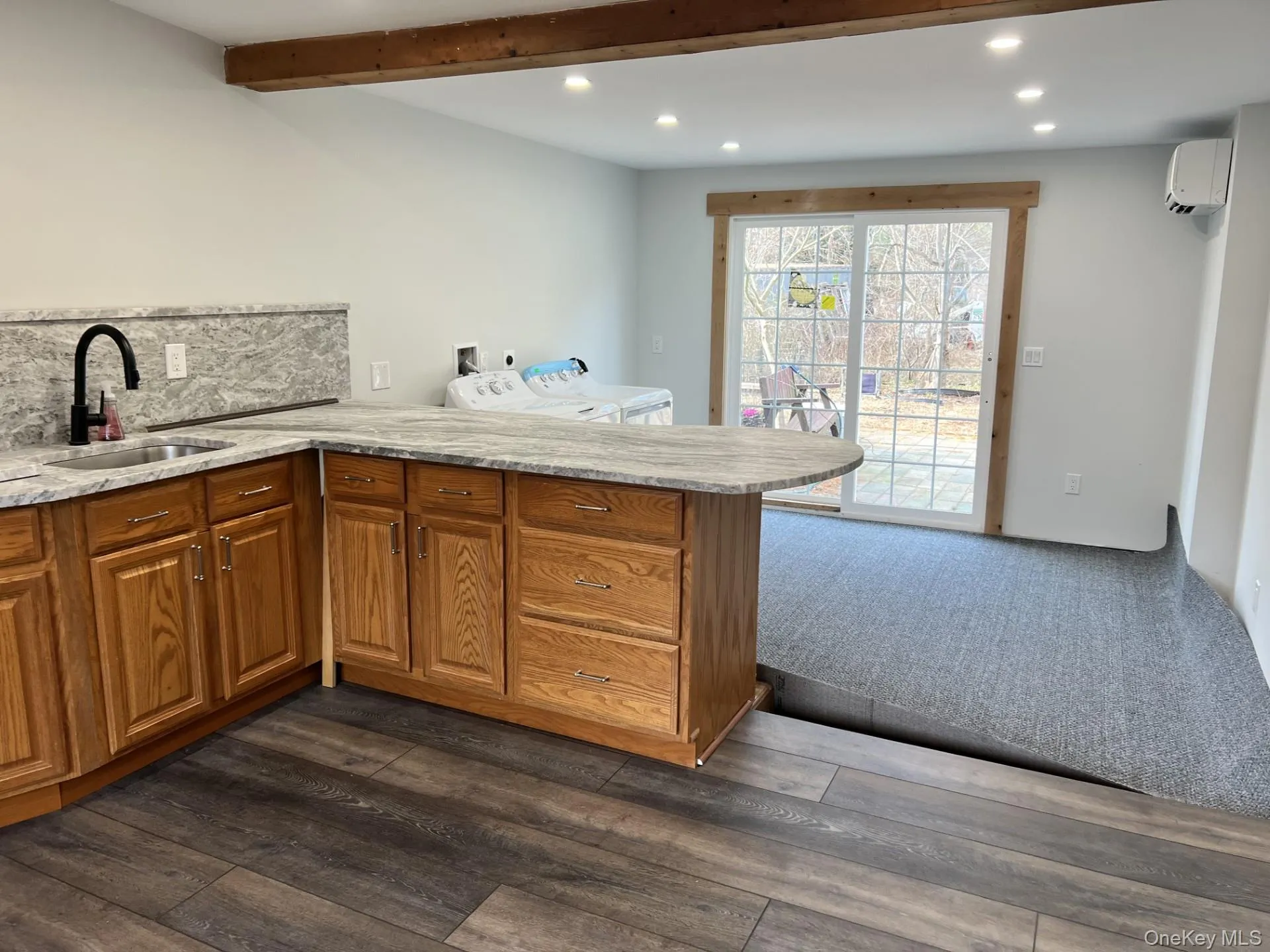 Kitchen featuring brown cabinets, recessed lighting, a peninsula, washer / clothes dryer, and a wall mounted air conditioner Kitchen featuring brown cabinets, recessed lighting, a peninsula, washer / clothes dryer, and a wall mounted air conditioner