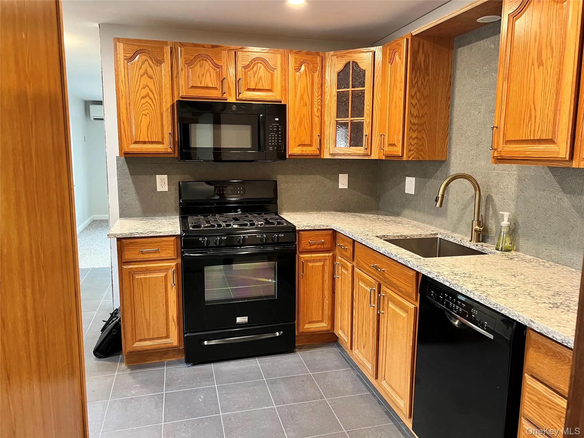 Kitchen featuring black appliances, dark tile patterned flooring, light stone countertops, and brown cabinets Kitchen featuring black appliances, dark tile patterned flooring, light stone countertops, and brown cabinets