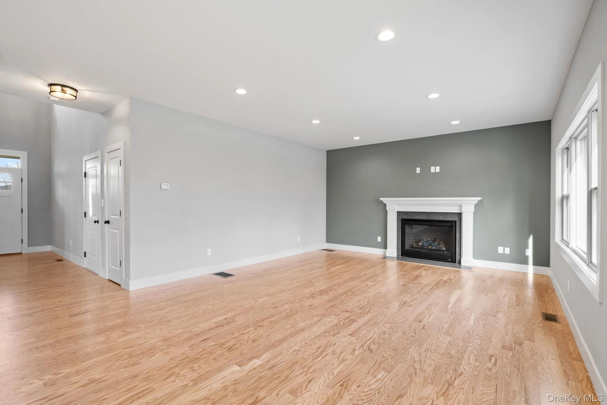 Unfurnished living room featuring healthy amount of natural light, recessed lighting, light wood finished floors, and a fireplace with flush hearth Unfurnished living room featuring healthy amount of natural light, recessed lighting, light wood finished floors, and a fireplace with flush hearth
