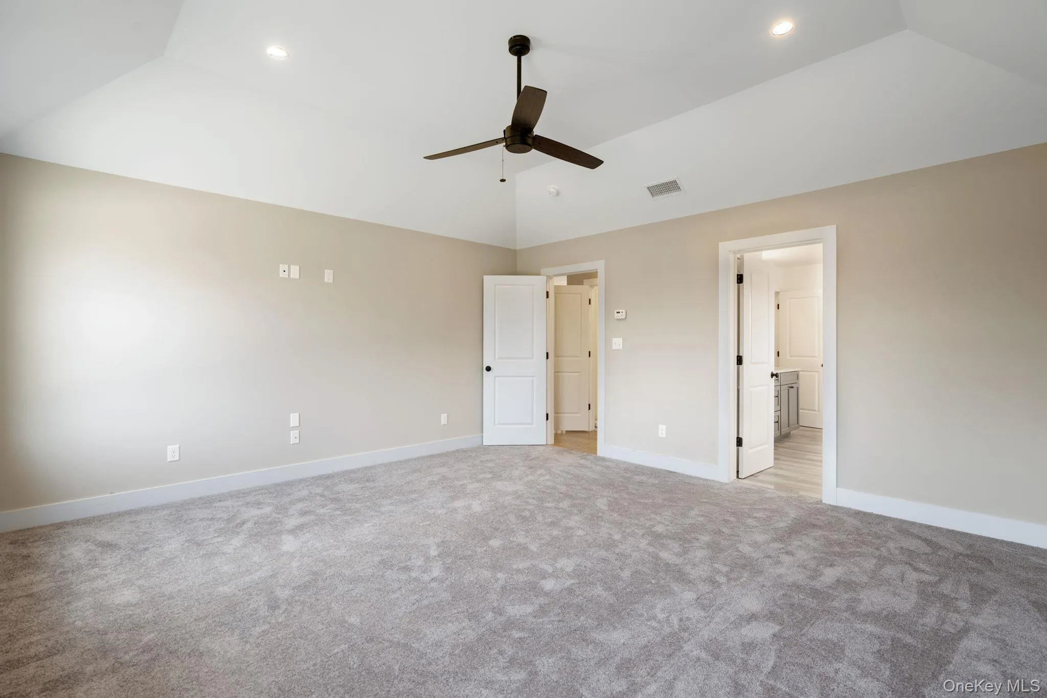 Unfurnished bedroom with vaulted ceiling, light colored carpet, ceiling fan, ensuite bathroom, and recessed lighting Unfurnished bedroom with vaulted ceiling, light colored carpet, ceiling fan, ensuite bathroom, and recessed lighting