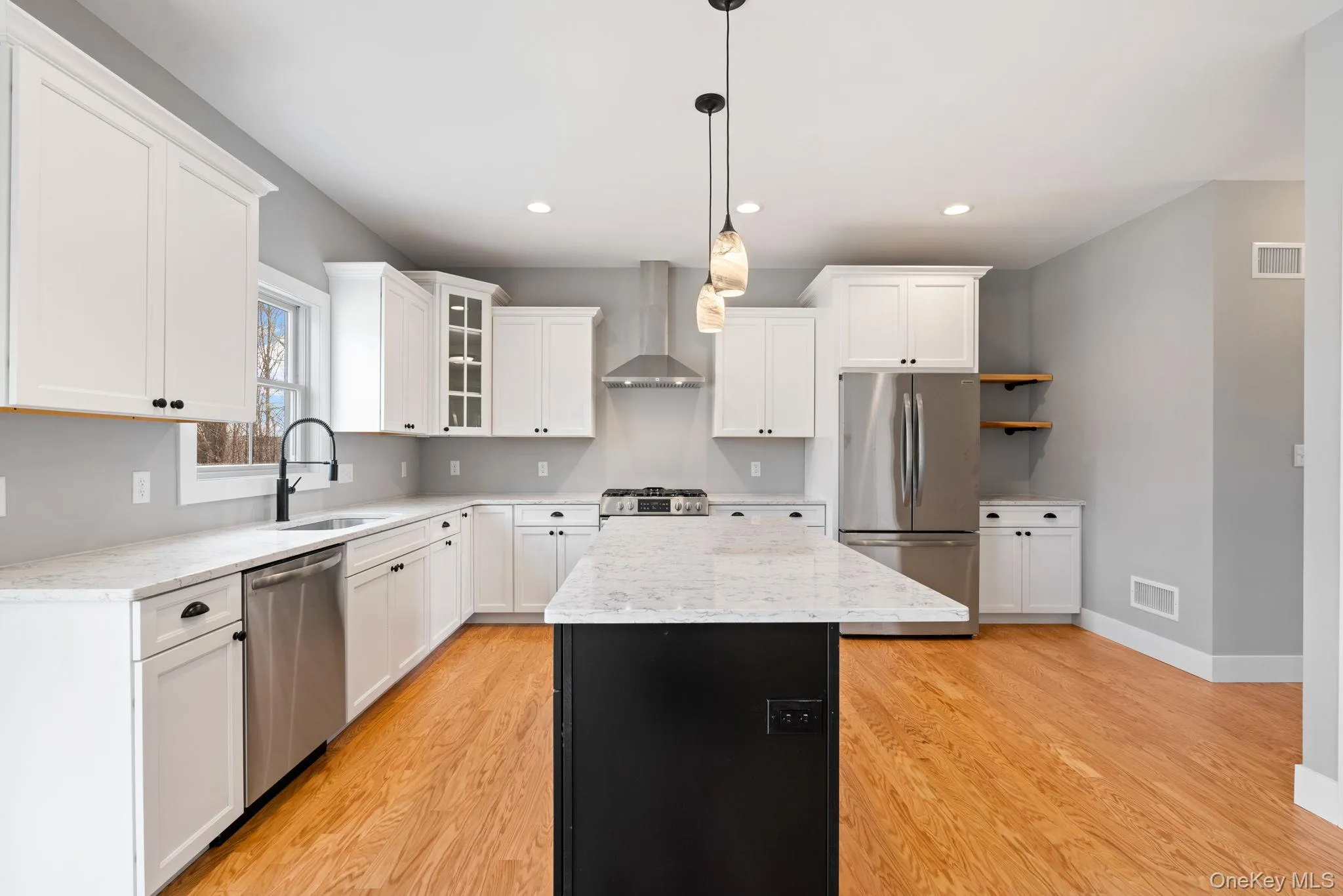 Kitchen featuring glass insert cabinets, stainless steel appliances, a kitchen island, white cabinets, and decorative light fixtures Kitchen featuring glass insert cabinets, stainless steel appliances, a kitchen island, white cabinets, and decorative light fixtures